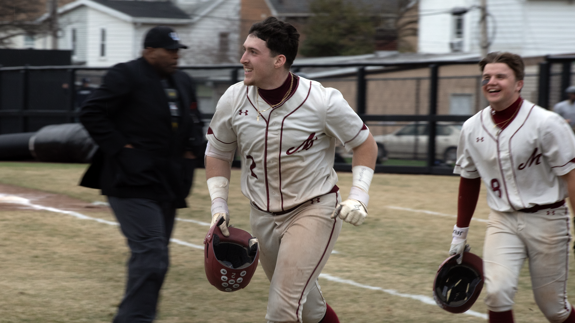 a baseball player in a white jersey smiling and holding his helmet in his right hand as he runs off the field