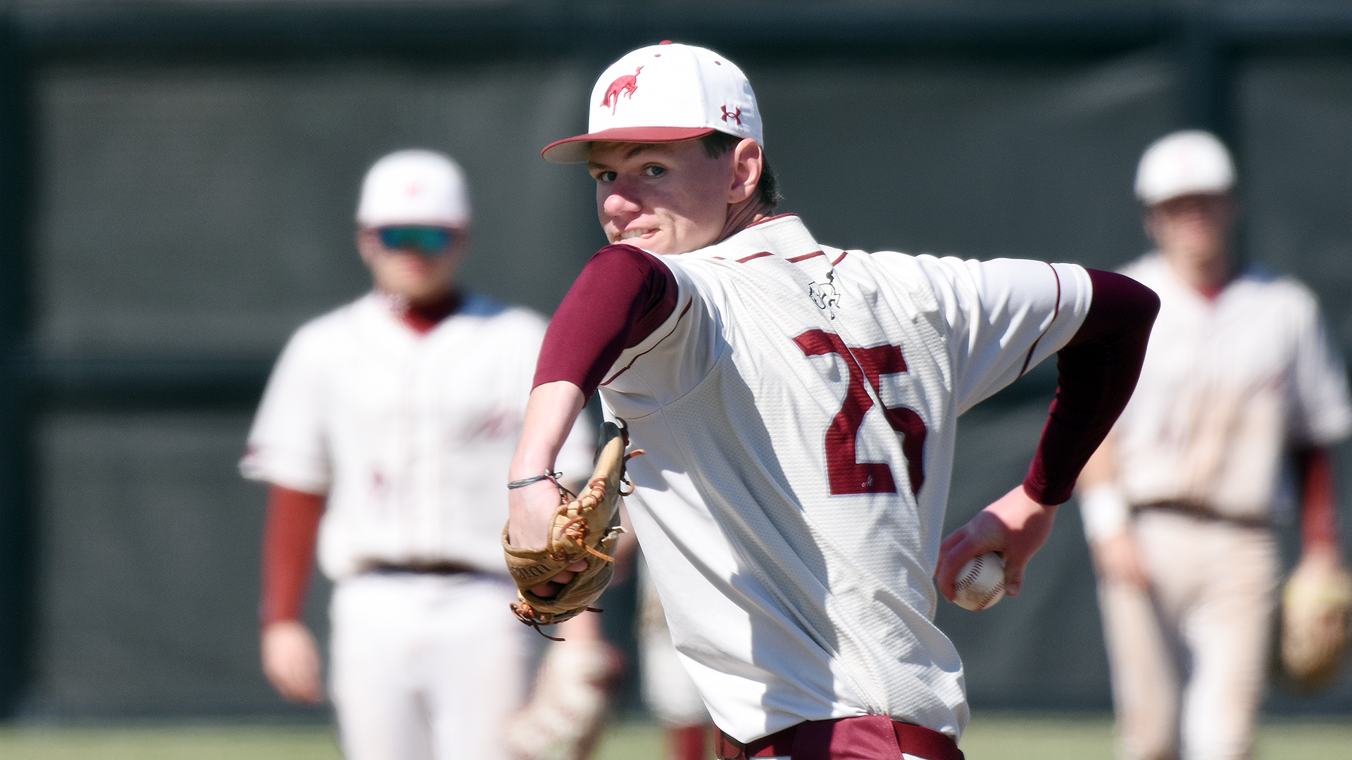 a baseball pitcher in a white jersey cocks his arm back
