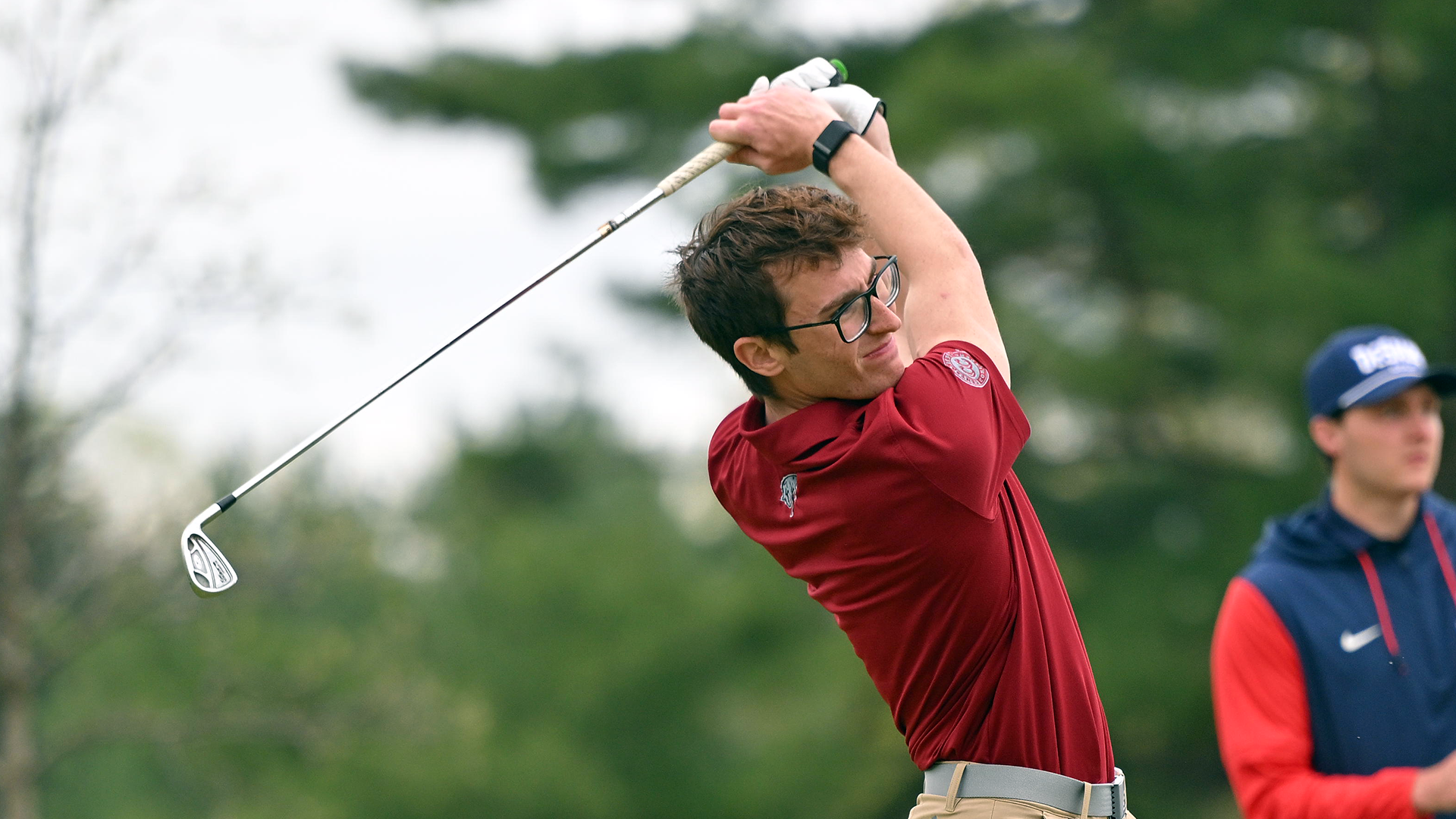 a golfer in a red shirt follows through on a shot hit with an iron