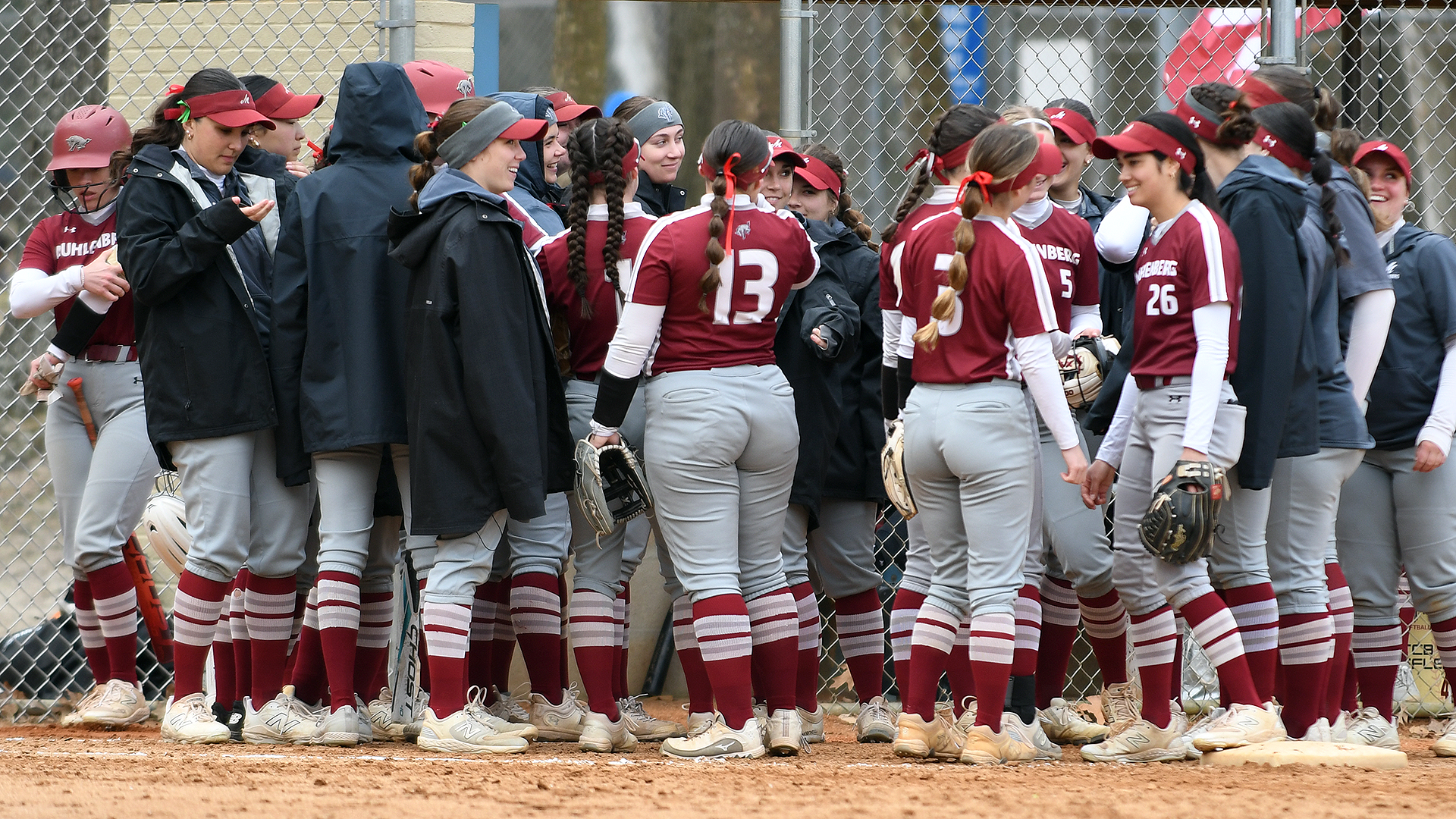 softball players in red uniforms and grey jackets huddling in a circle