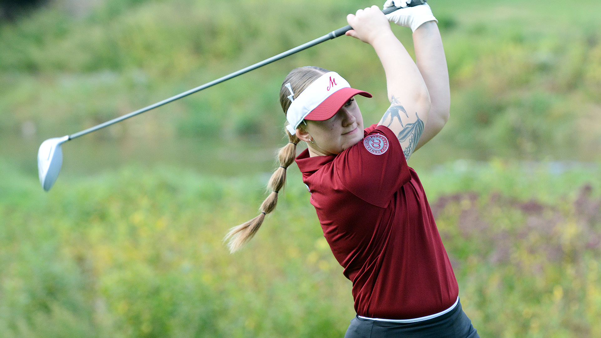 a women's golfer in a red shirt follows through after hitting an iron
