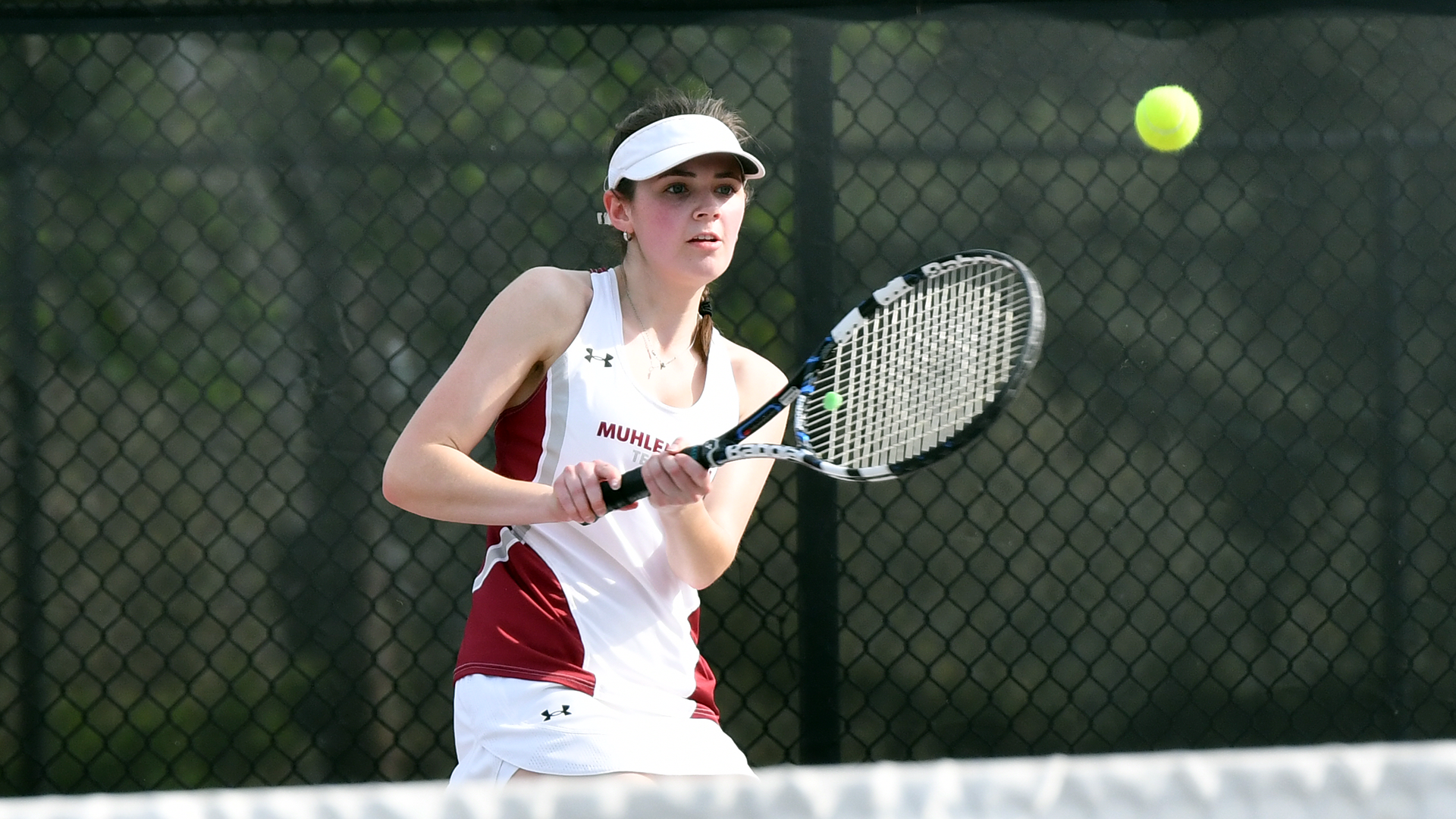 a tennis player in a white shirt and white visor follows through on a backhand shot