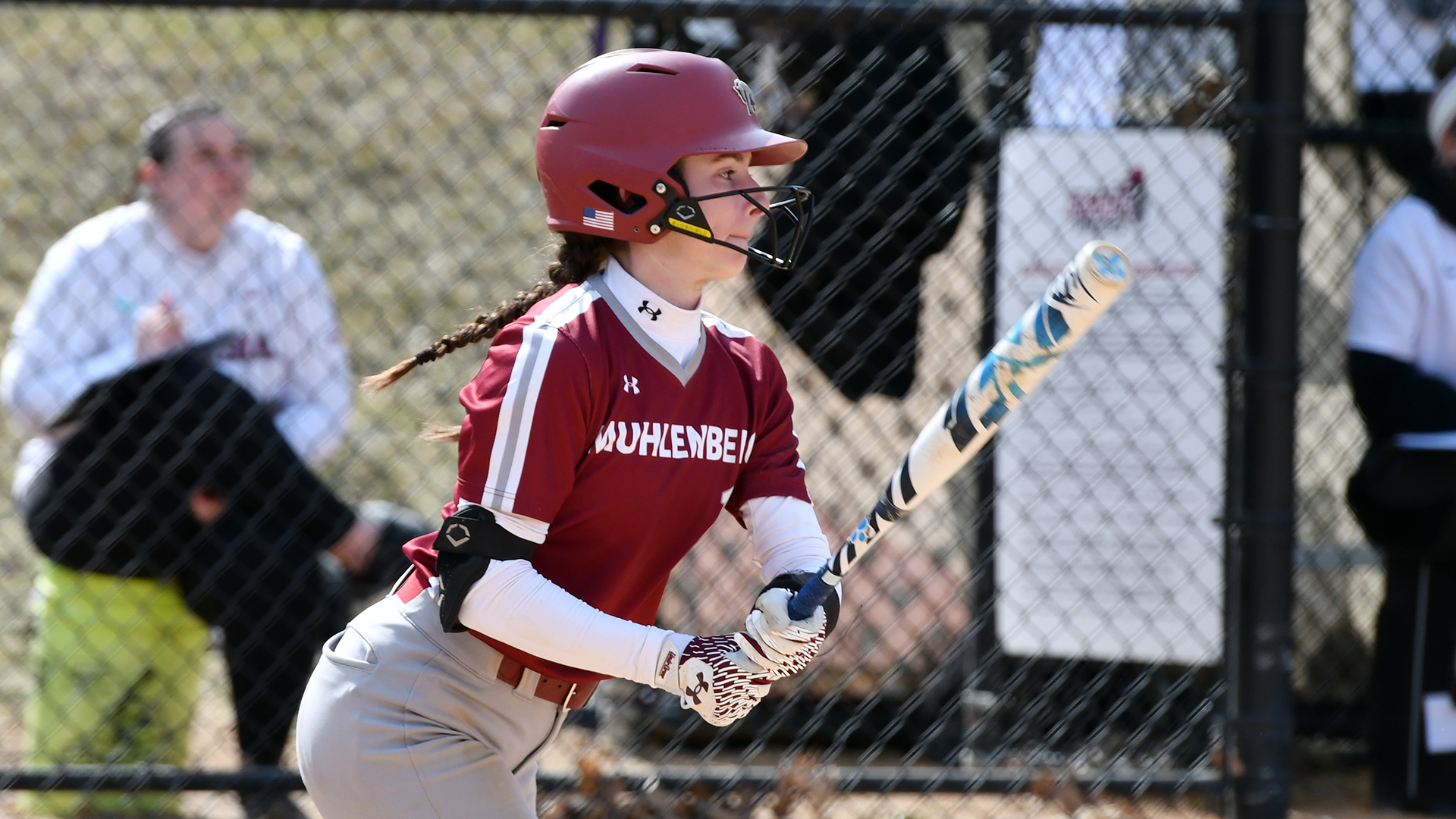 a left-handed softball batter in a red jersey and red helmet follows through on a swing