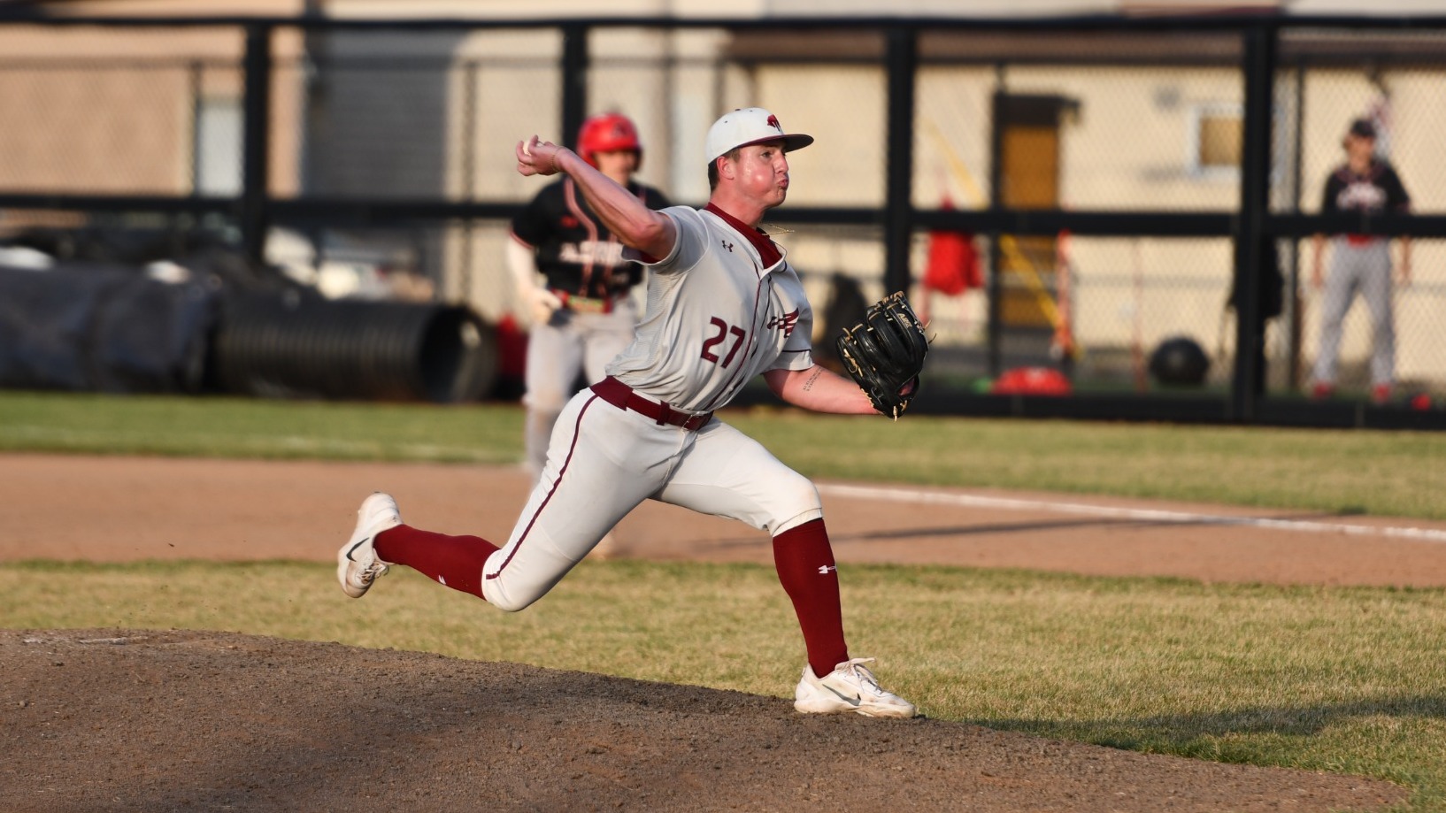 A pitcher in a white uniform throws a pitch on a baseball field