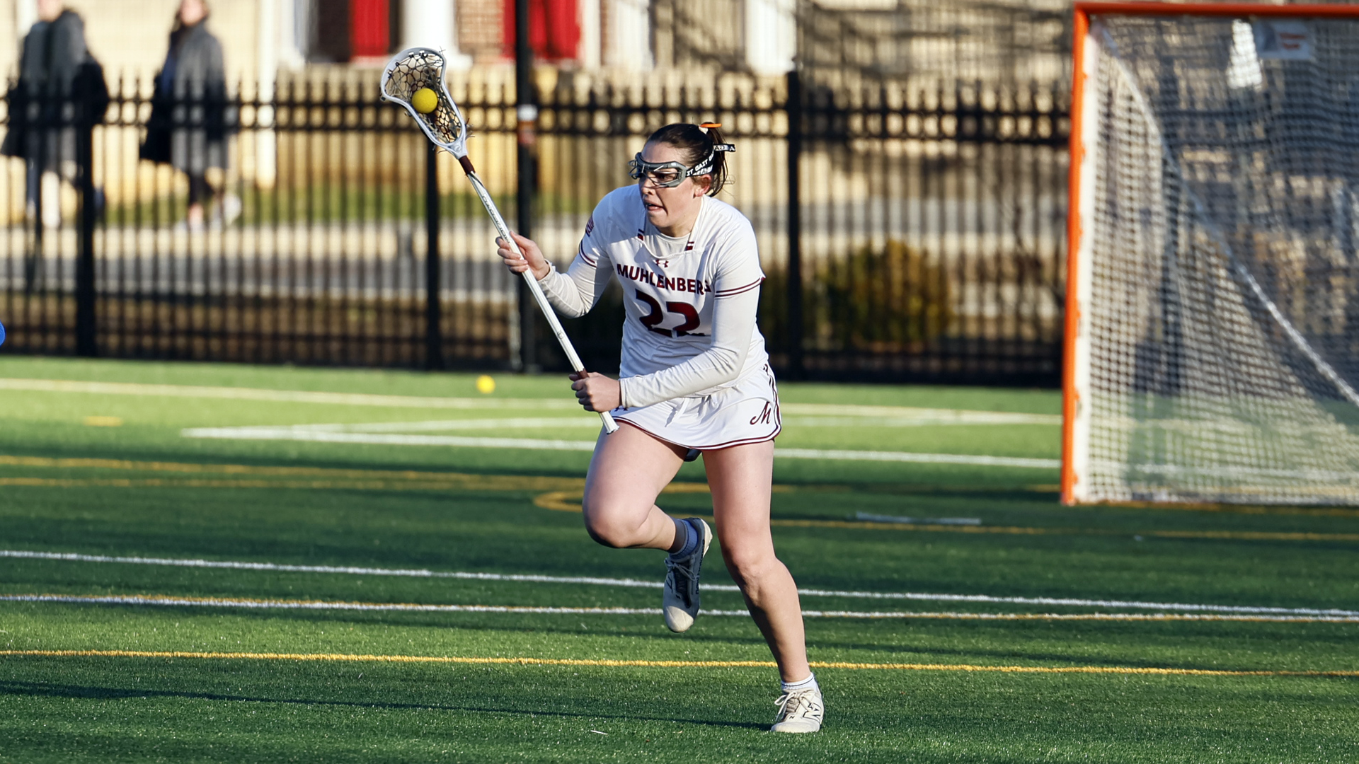 a women's lacrosse player in a white uniform bringing the ball up the field