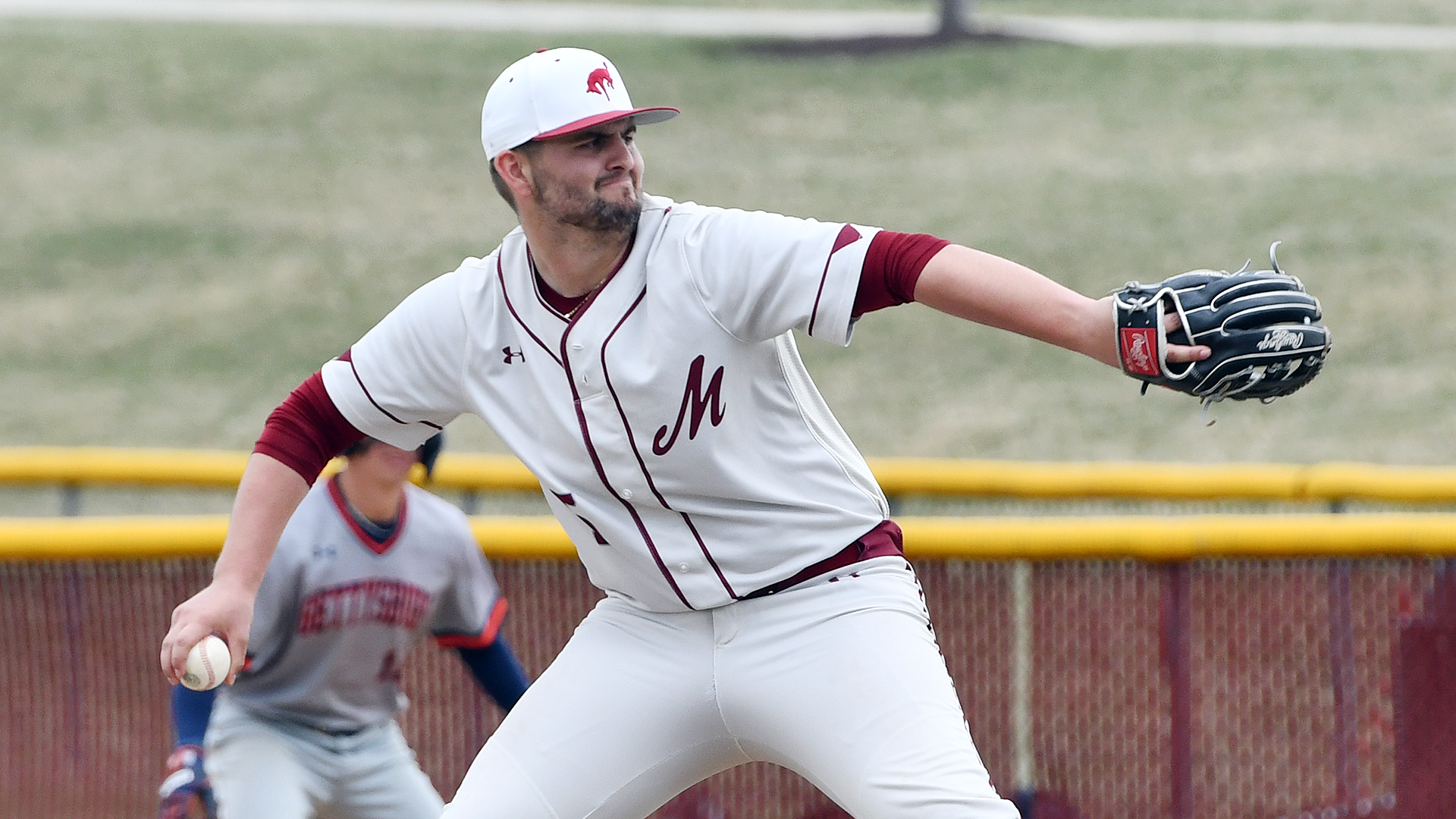 a right-handed baseball pitcher in a white jersey and white hat cocking his arm back to deliver a pitch
