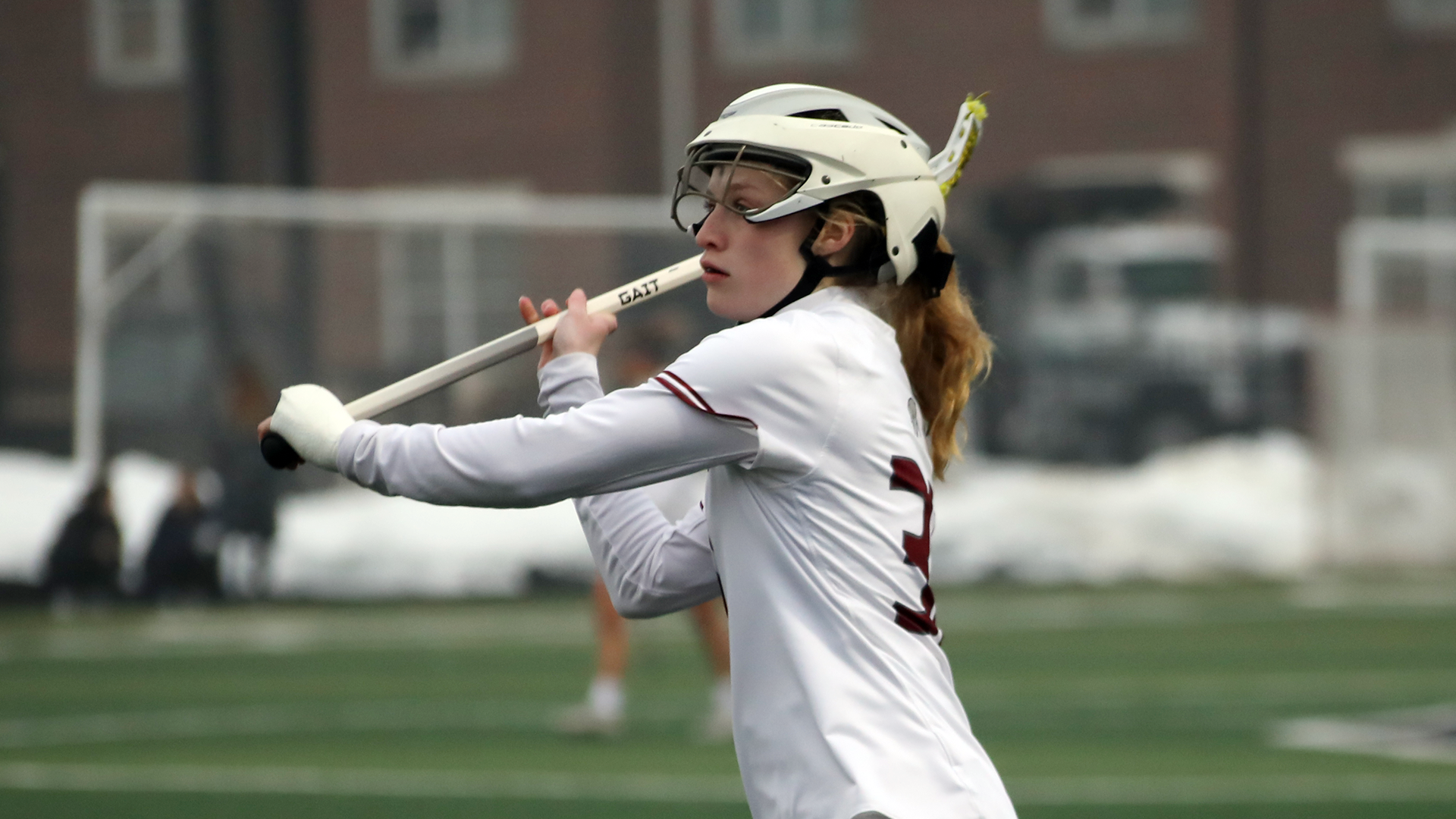 a women's lacrosse player in a white jersey and white helmet bringing the stick behind her shoulder to make a pass