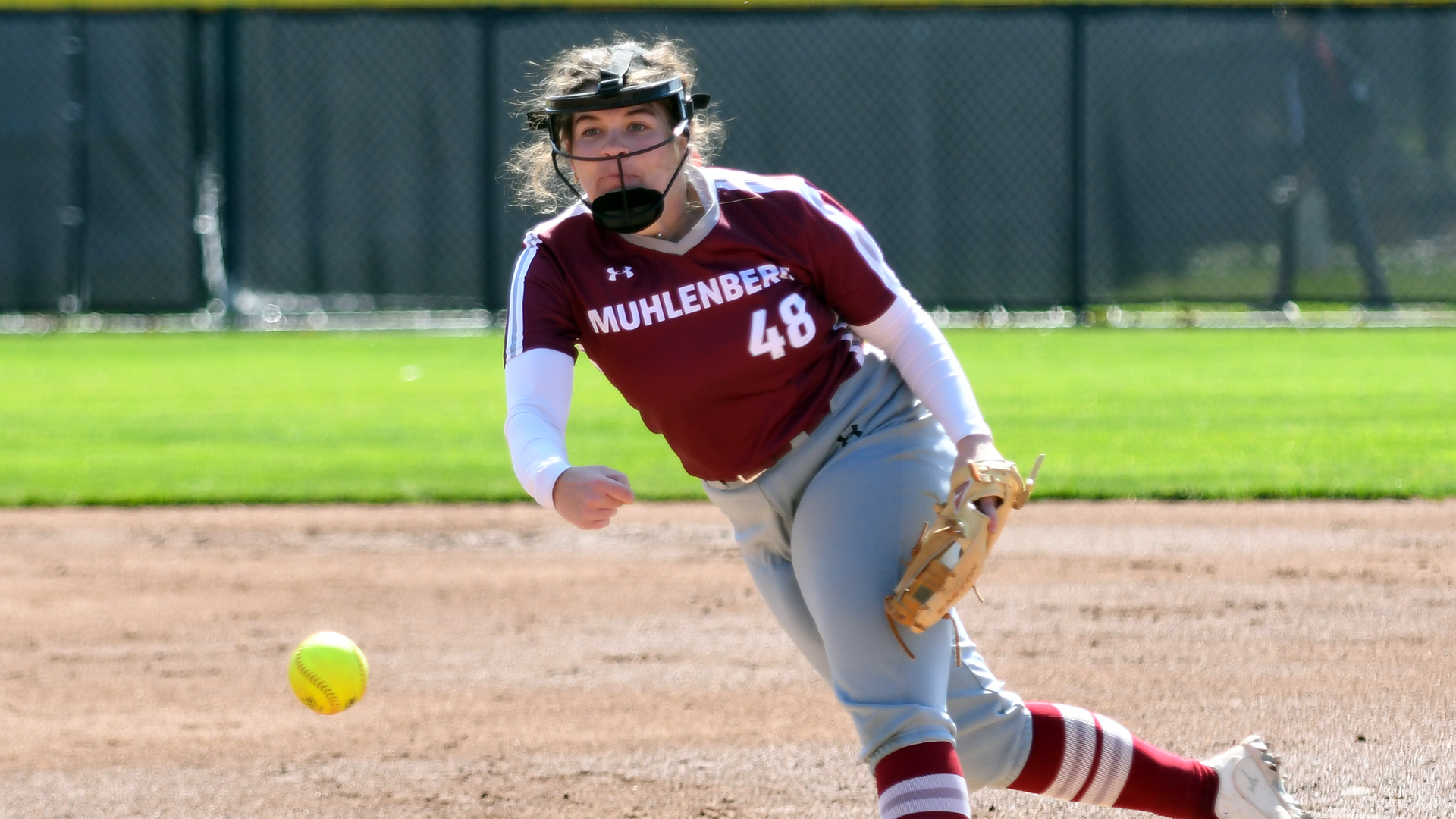 a softball pitcher in a red uniform delivering the ball to the plate