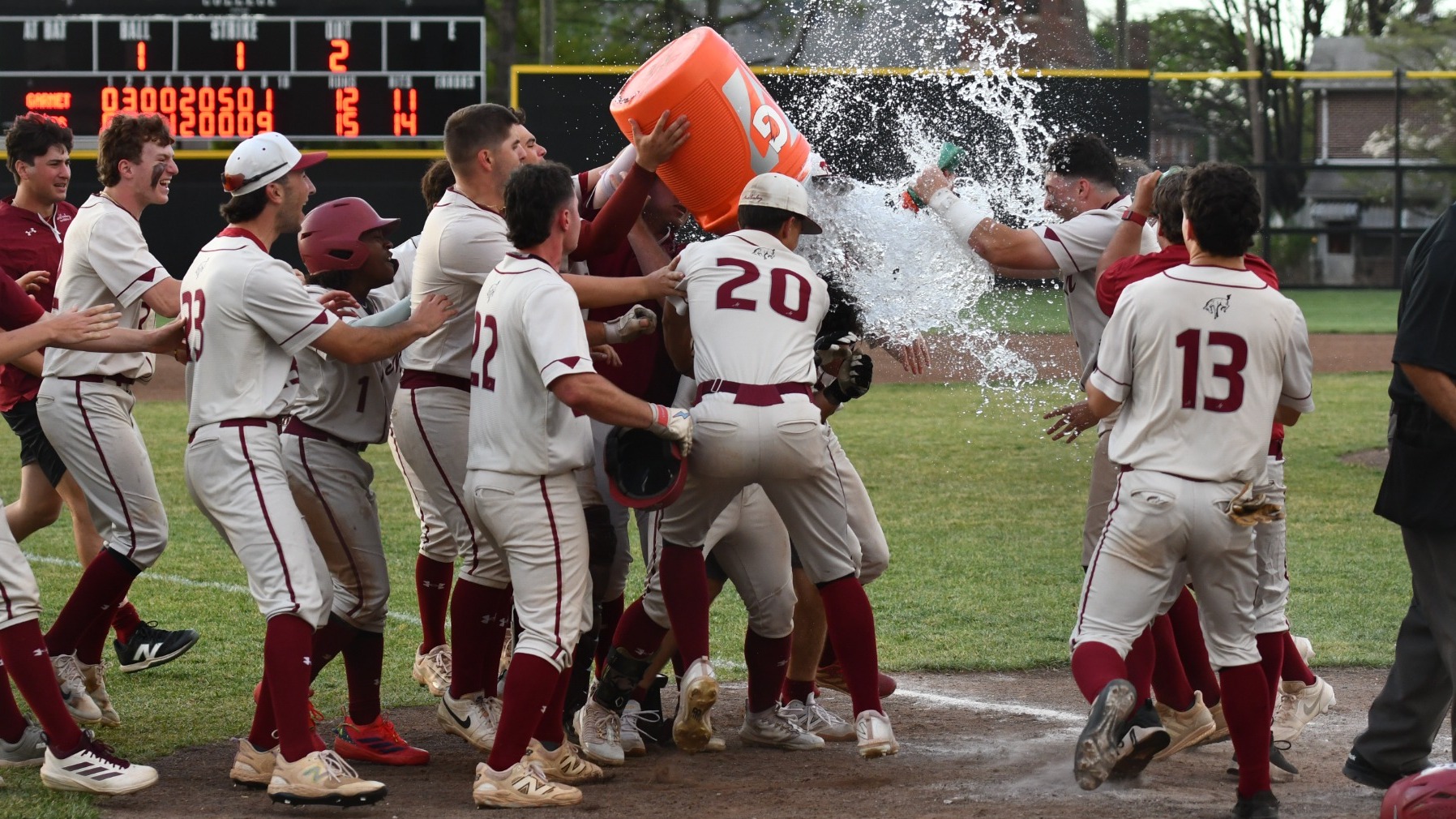 A group of baseball players surround one player as they dump a water cooler on him in celebration