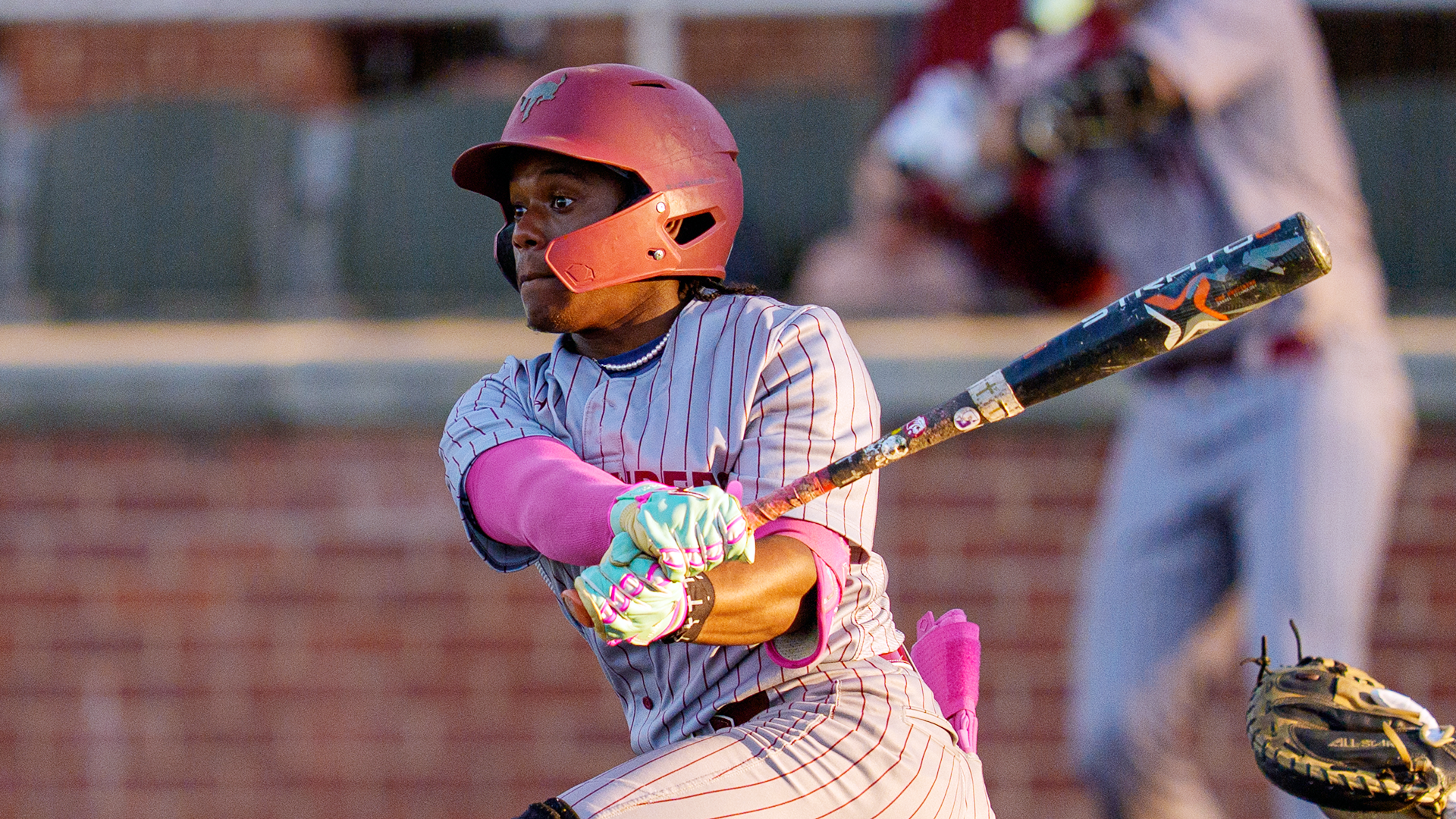 a baseball player in a grey pinstriped jersey and red helmet watching the path of the ball after swinging