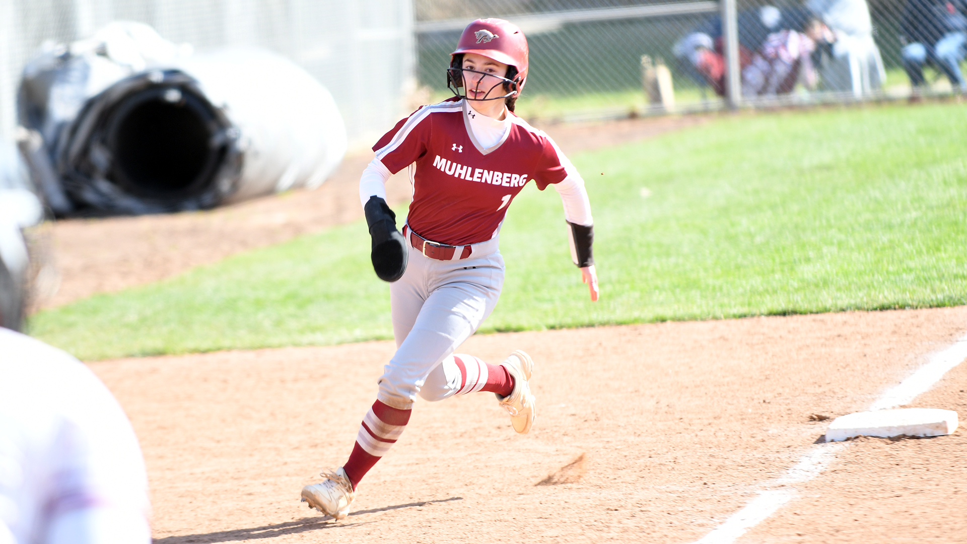 a softball player in a red top and white pants rounding third base