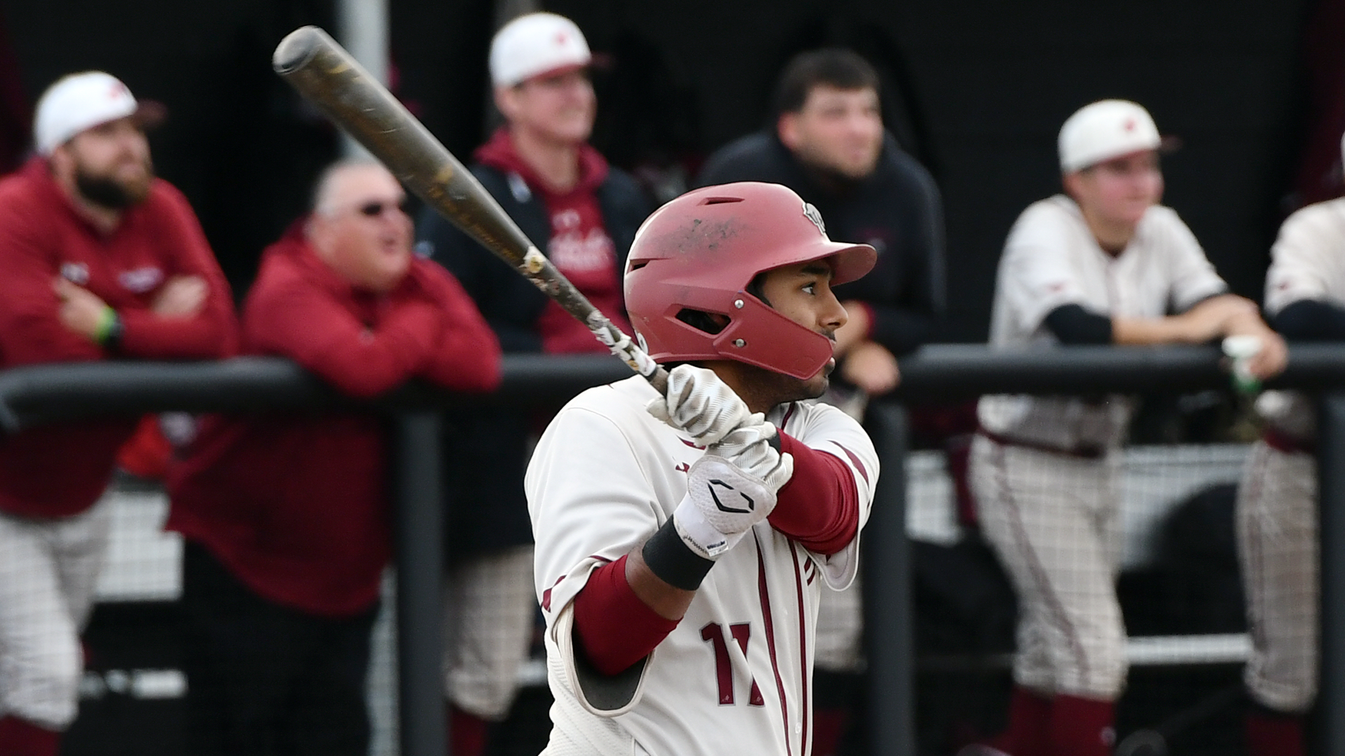 a baseball player in a white uniform and red helmet following through on his swing