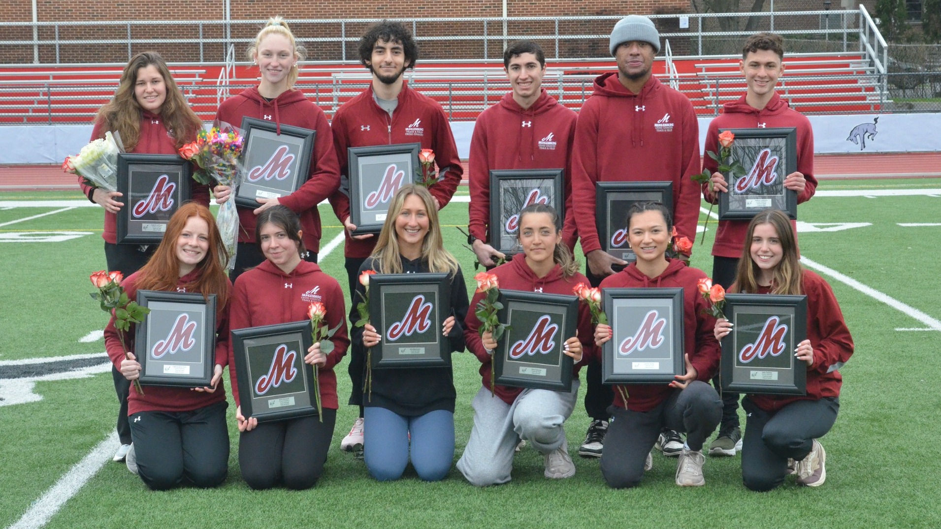 12 senior student athletes pose for a photo wearing red and holding black plaques