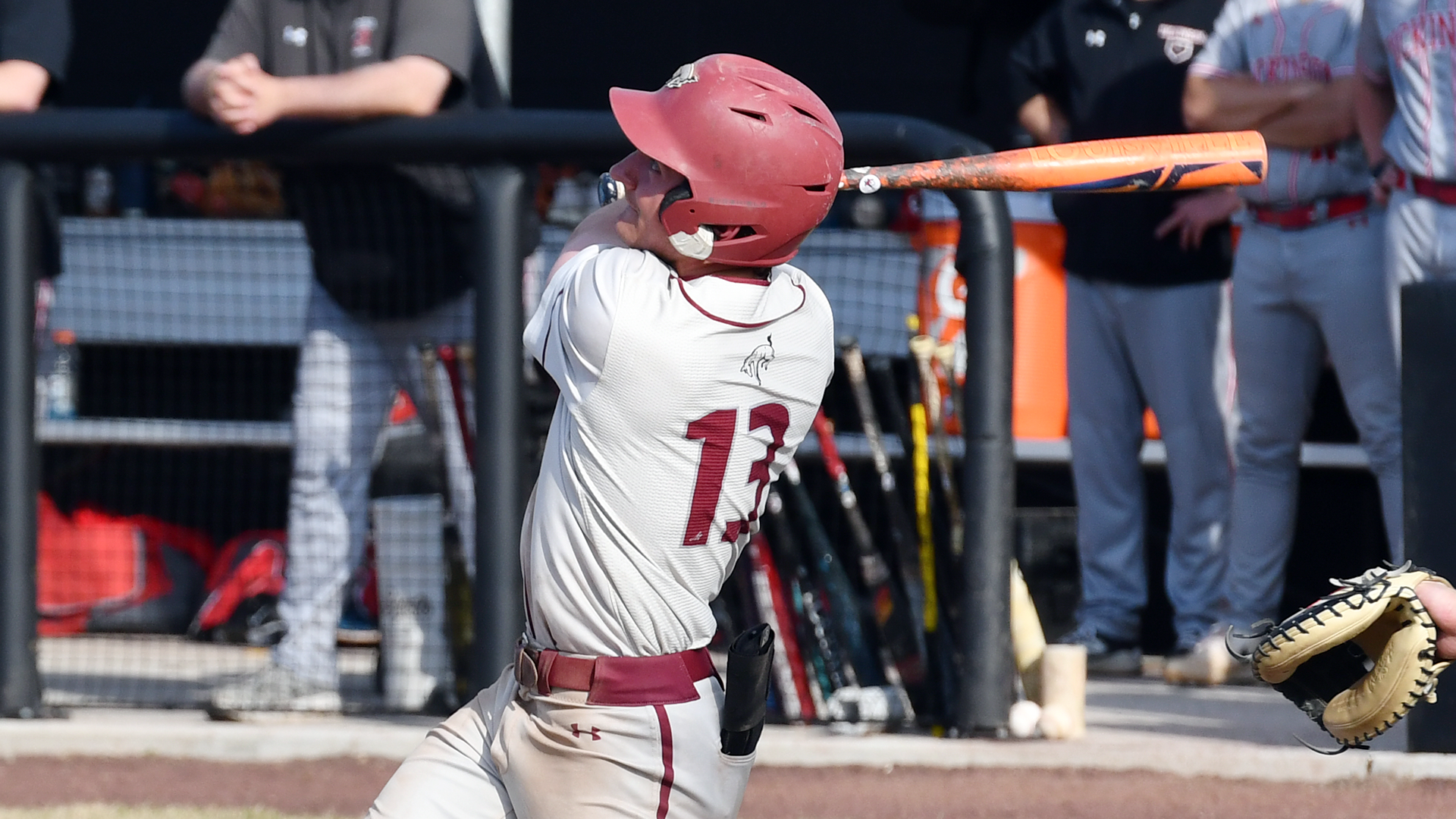 a left-handed baseball hitter in a white jersey and red helmet follows through on his swing