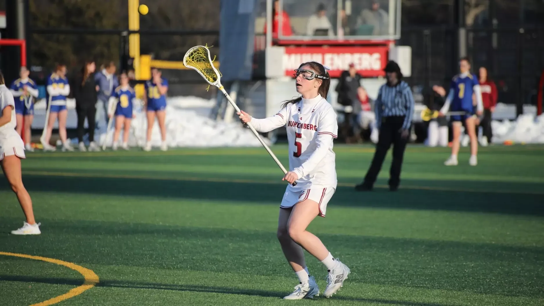 A Muhlenberg women’s lacrosse player wearing #5 in white catches a pass from a teammate.