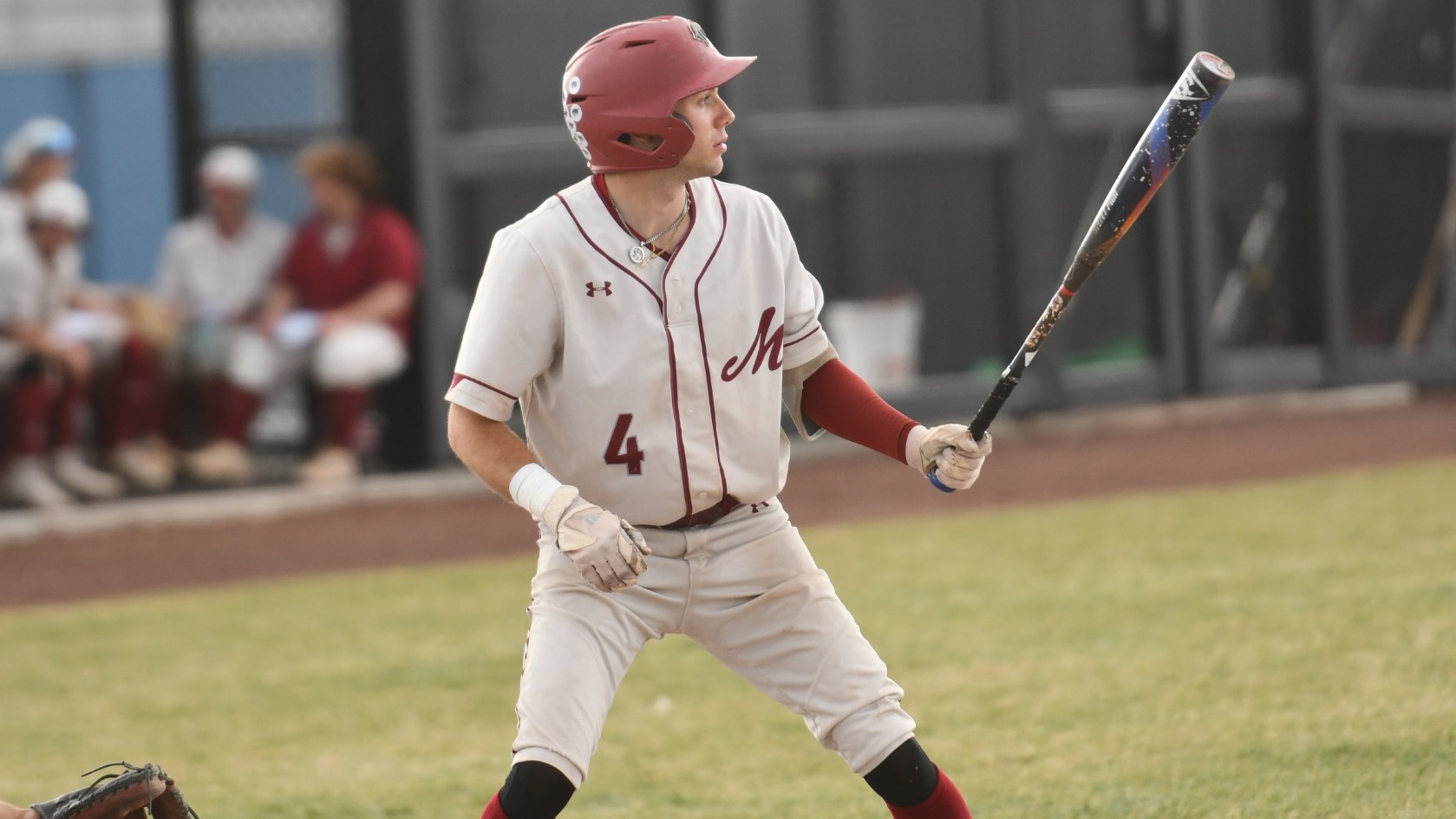 A baseball player in a white uniform points his bat at the pitcher in the batters box