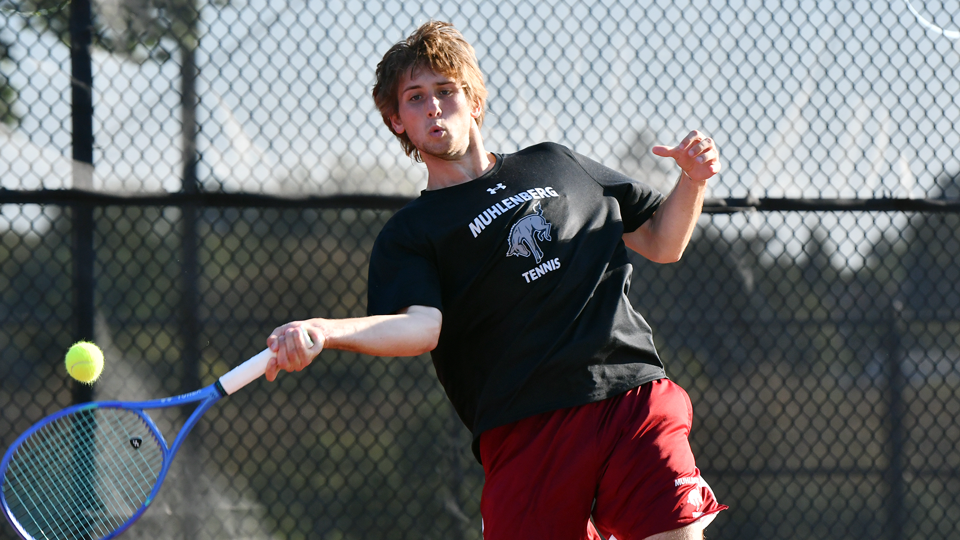 a men's tennis player in a black t-shirt and red shorts hitting a forehand