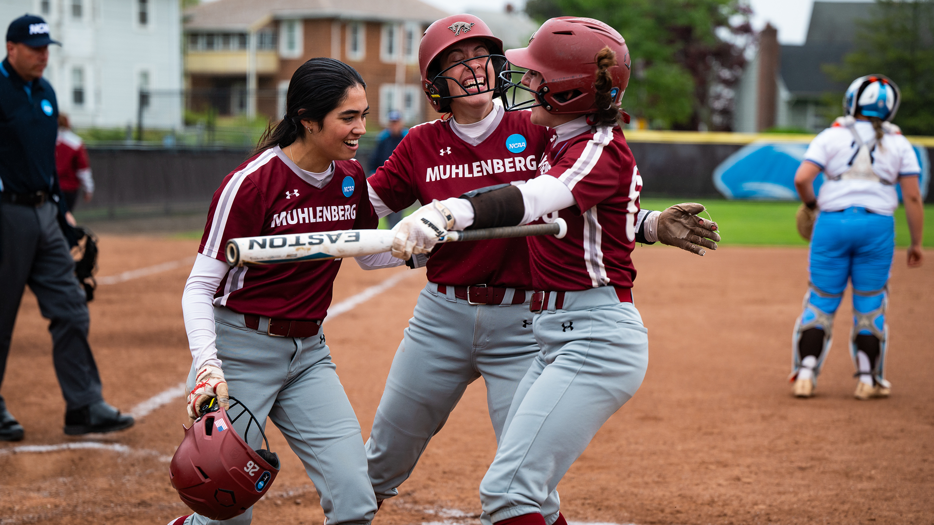 three softball players in red jerseys celebrating at home plate