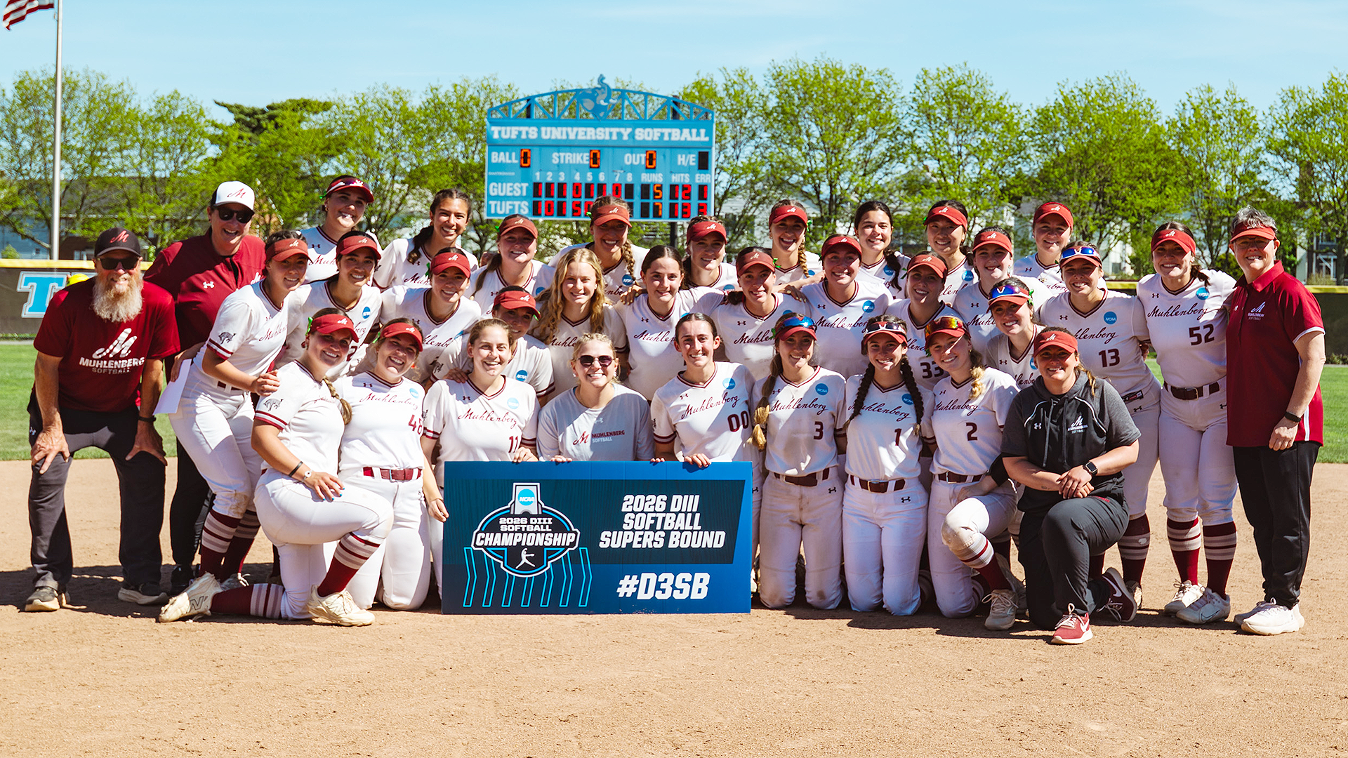 a softball team in white uniforms posing front of a scoreboard and holding a sign that reads 2026 DIII Softball Supers Bound