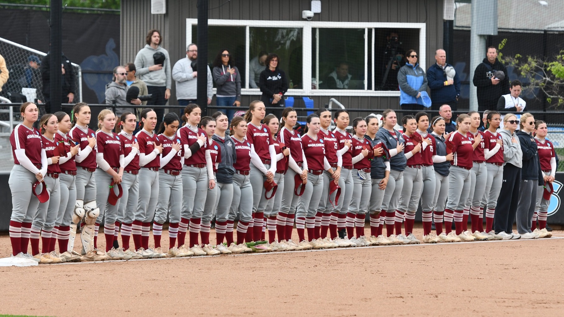 Softball players in red and gray uniforms line up for the national anthem