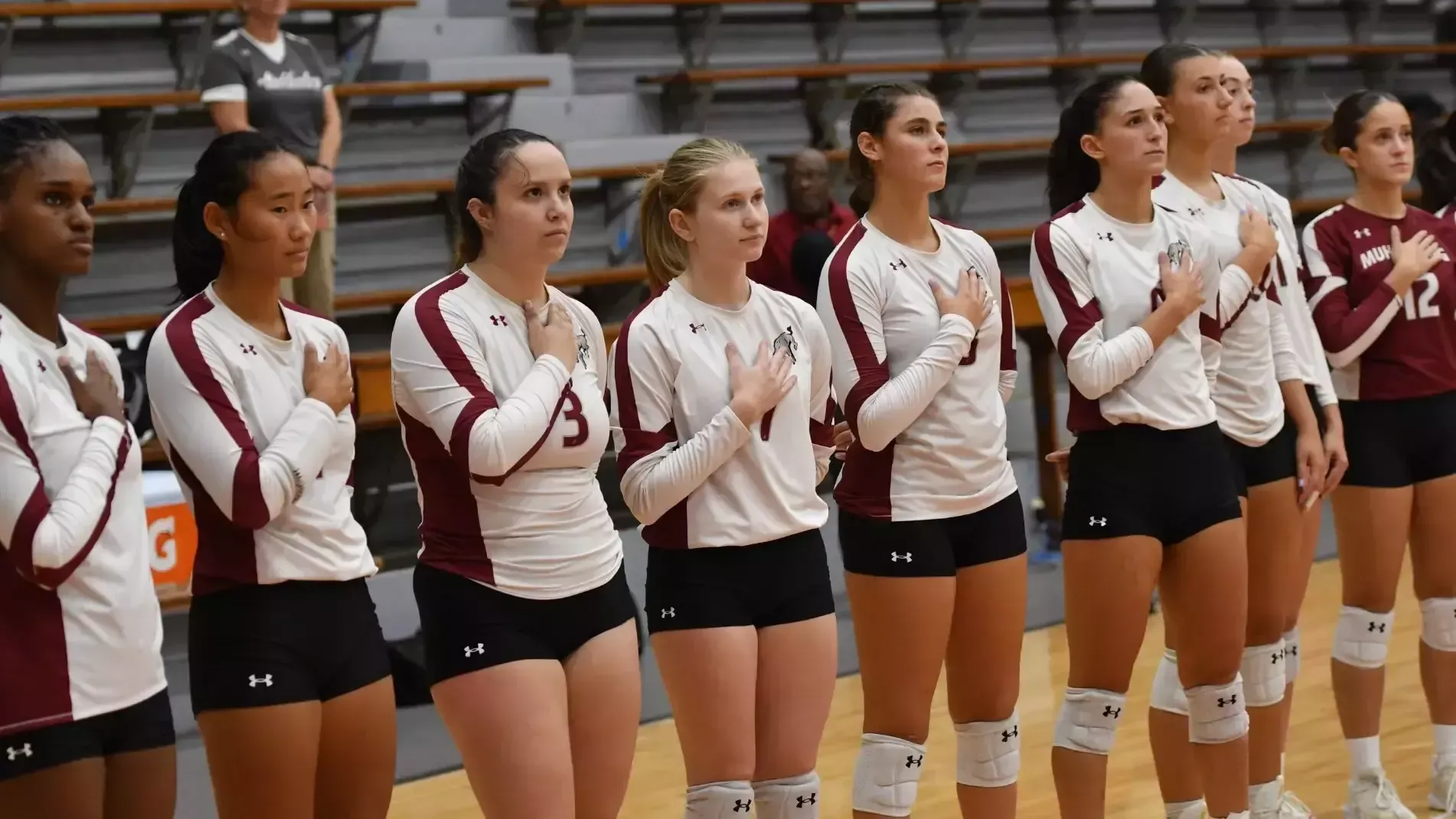 Volleyball players stand respectfully for the national anthem in a gymnasium 
