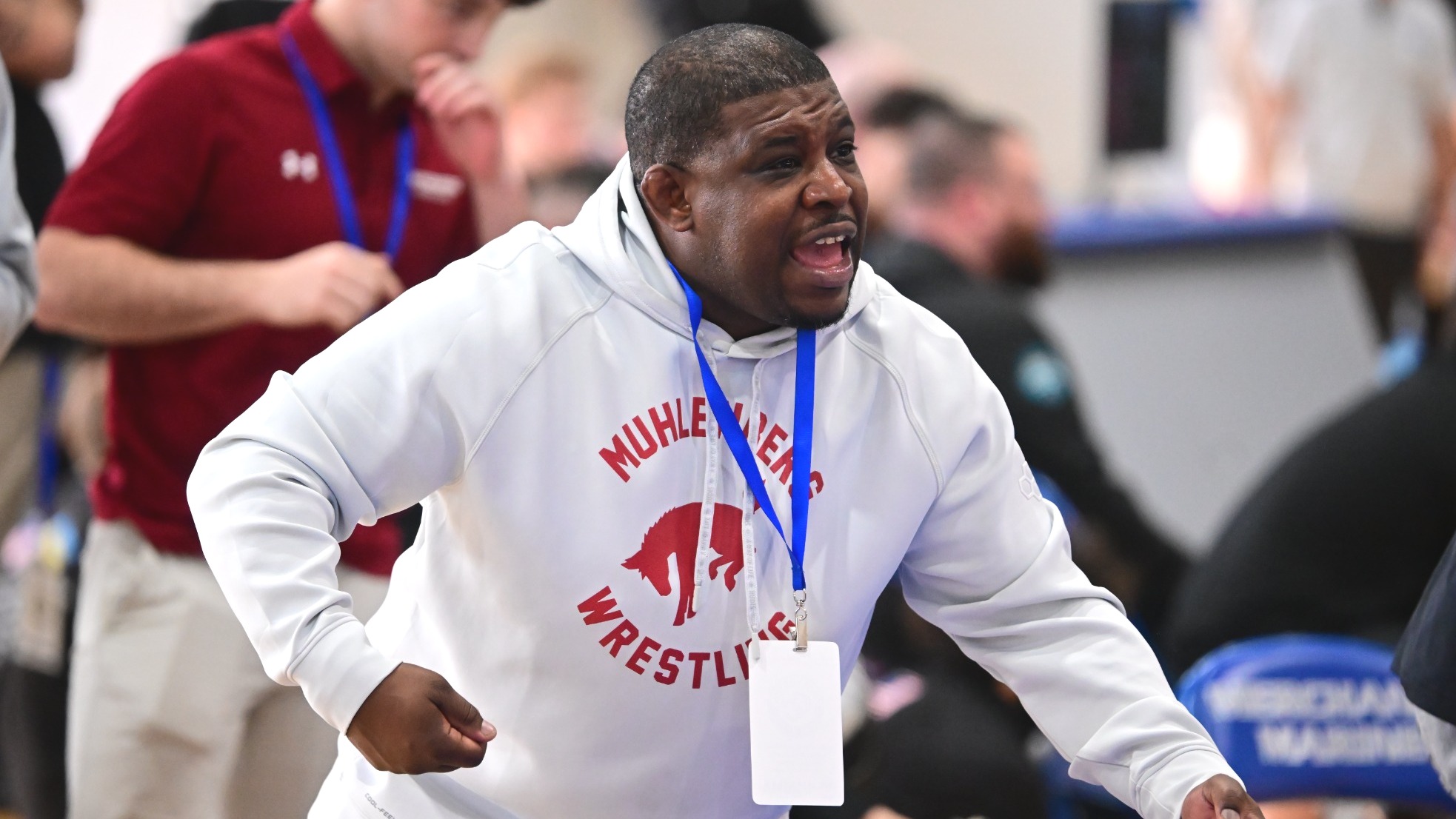 A coach in a white sweatshirt gestures at his wrestlers while coaching a match