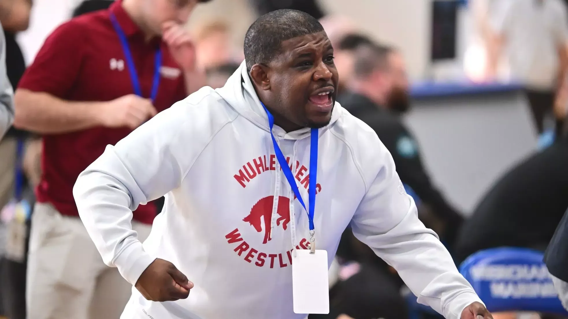 A coach in a white sweatshirt gestures at his wrestlers while coaching a match
