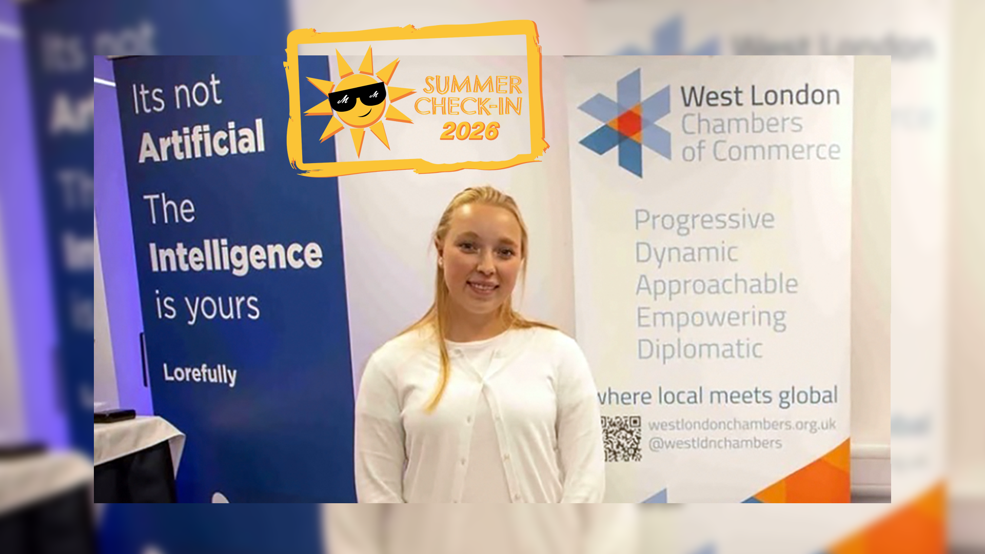 a young woman in a white sweater posing in front of a West London Chambers of Commerce banner