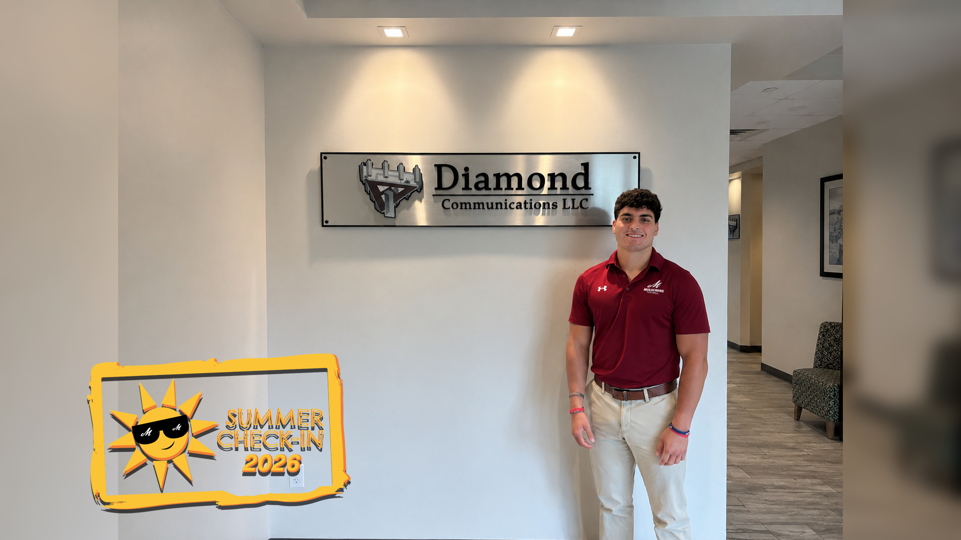 a young man in a maroon polo shirt and beige slacks standing in front of a Diamond Communications LLC wall sign 