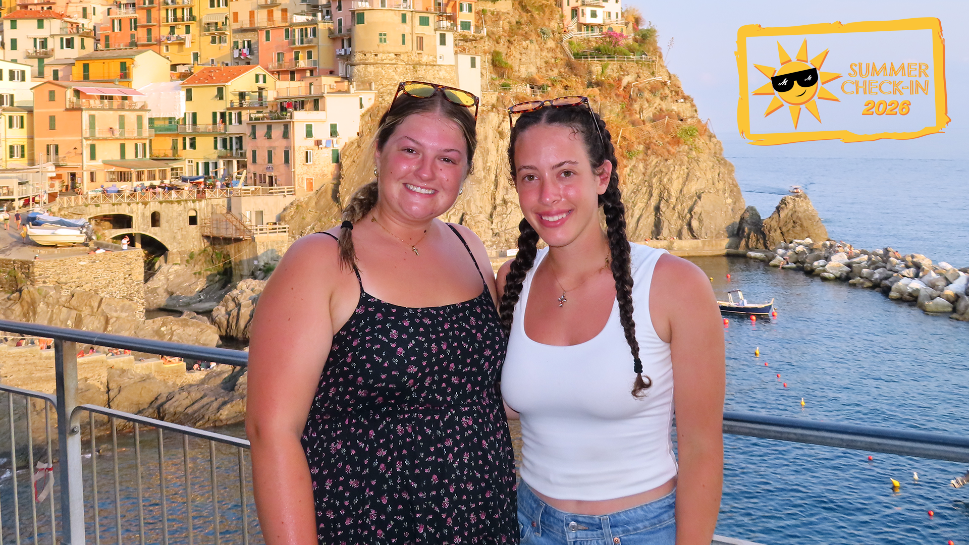 two young women on the Italian seaside, with houses behind them on the left and water on the right