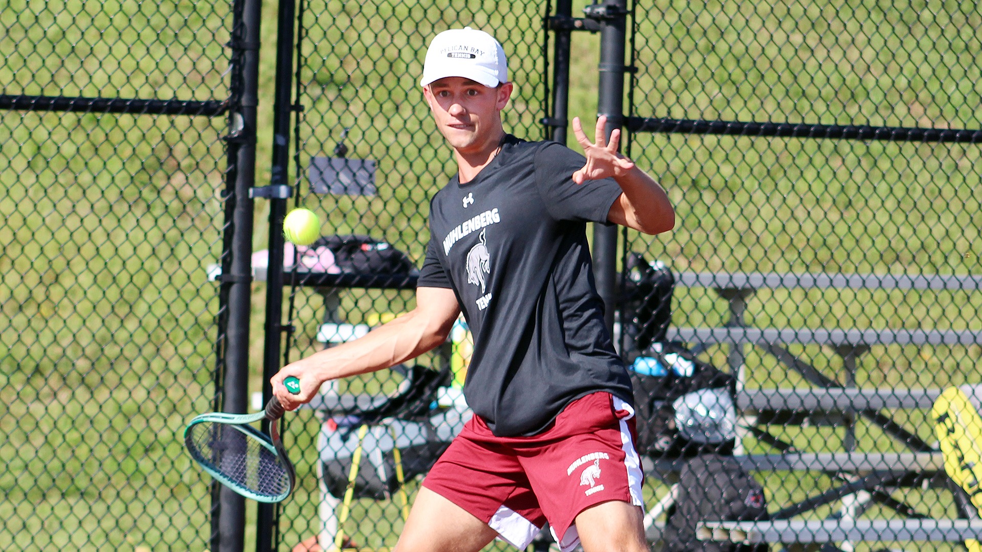 a tennis player in a white cap, black t-shirt and red shorts hitting a forehand