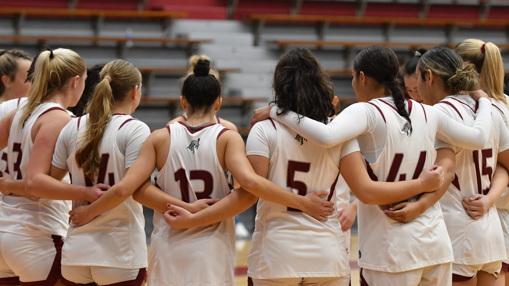 A women's basketball team in white uniforms huddles up
