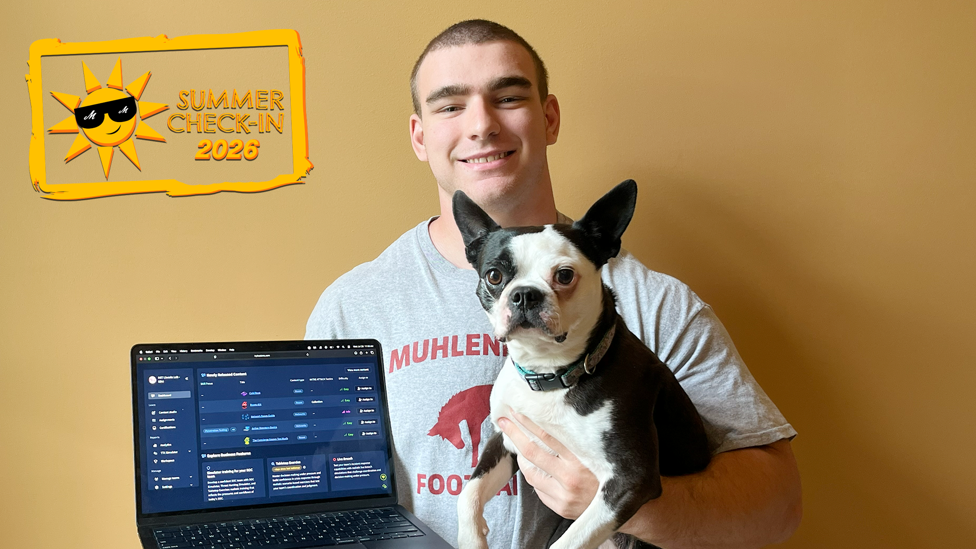 a man in a grey t-shirt with a laptop in one hand and a black-and-white dog in the other