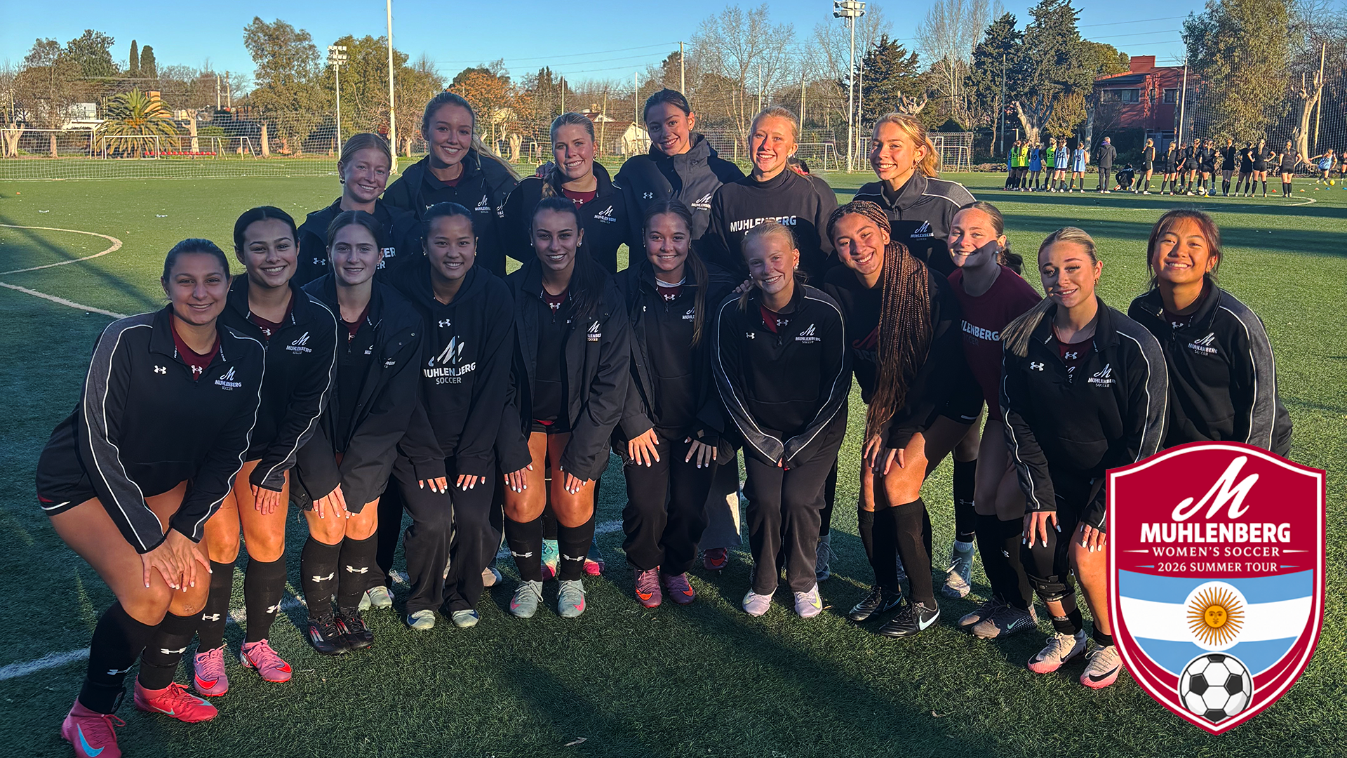 women's soccer players in black warmup suits posing for a group photo on a soccer field