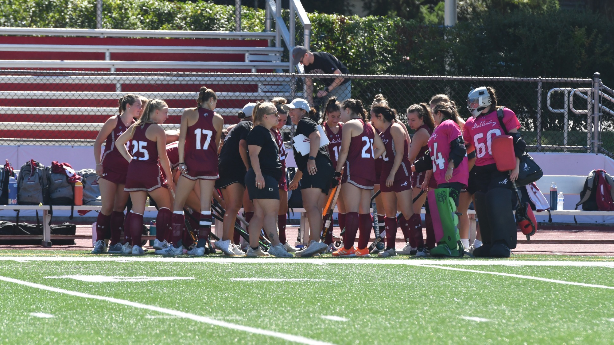 A team of field hockey players dressed in red huddles to discuss on the sidelines