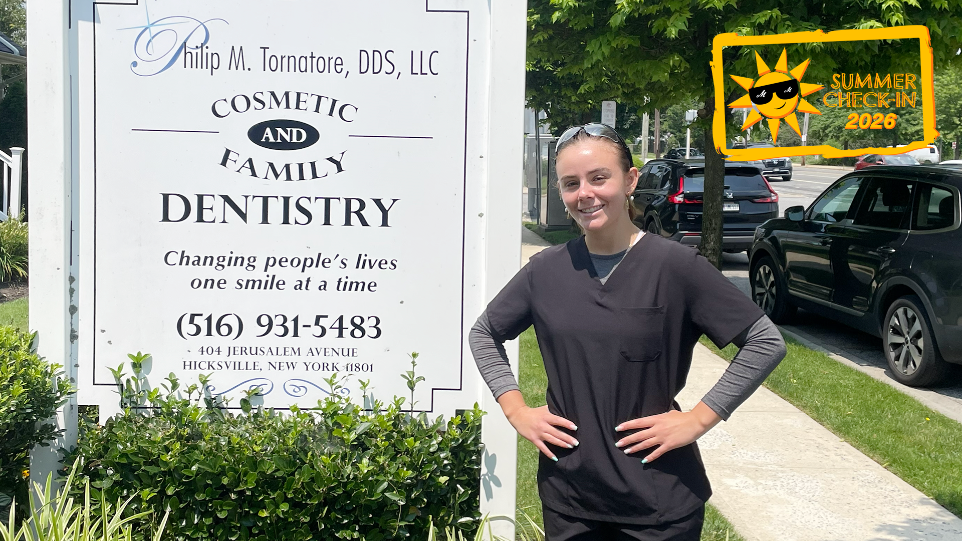 a woman in a black doctor's outfit posing outdoors next to a white sign reading Philip M. Tornatore, DDS, LLC Cosmetic and Family Dentistry