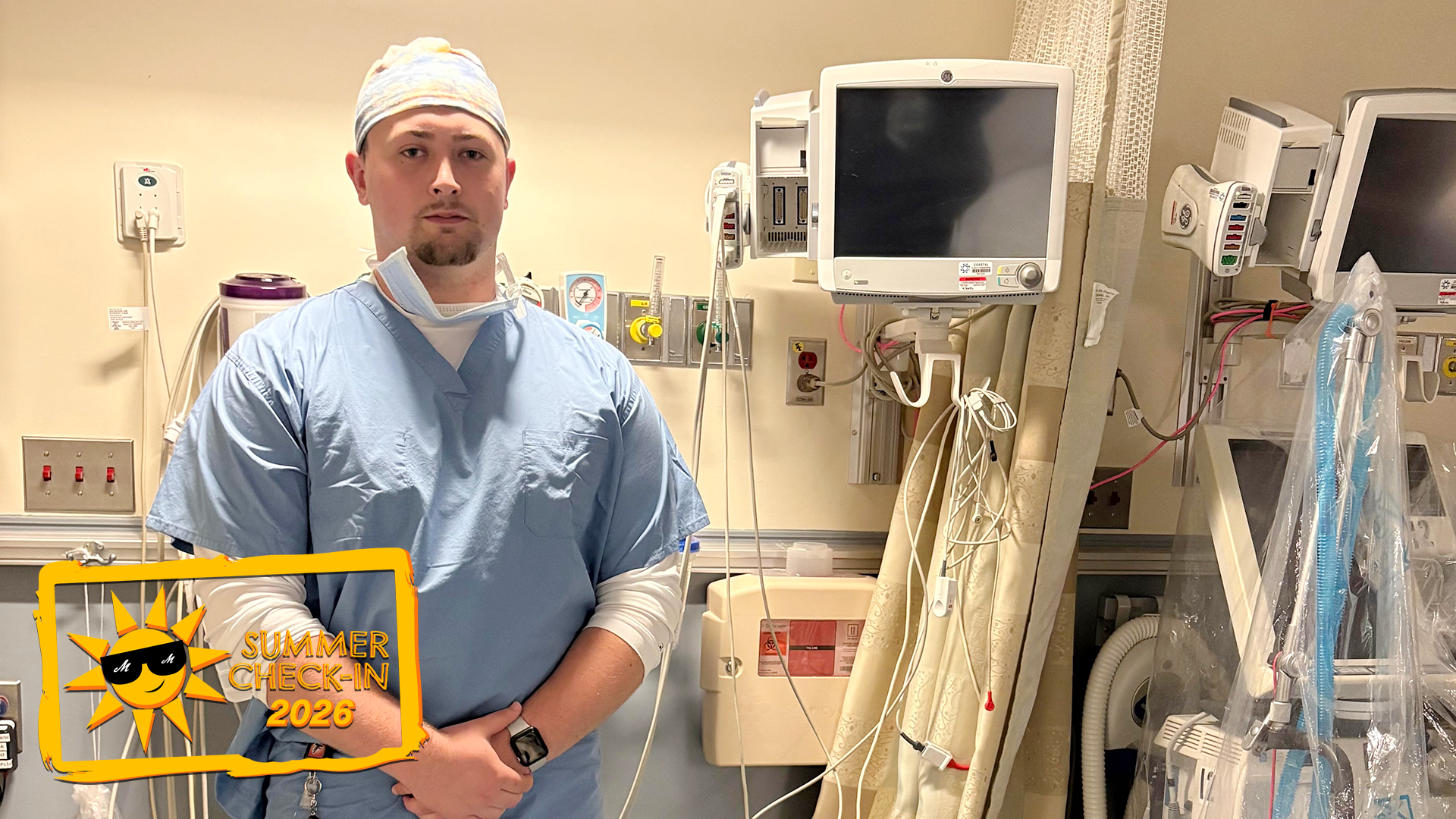 a young man in light blue scrubs standing in a hospital room filled with medical equipment