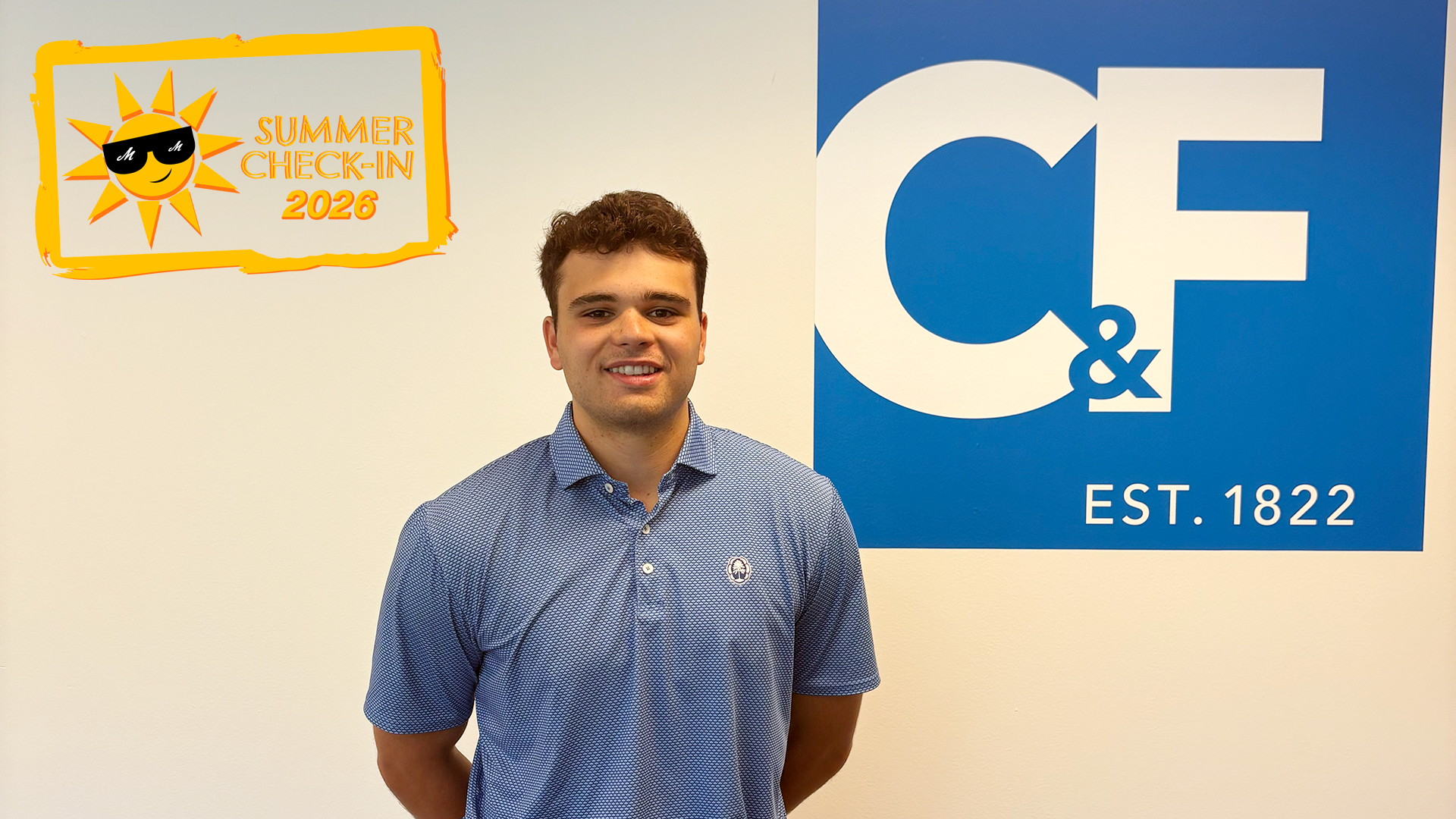 a young man in a blue polo shirt standing in front of a white wall with a blue square logo with the letters C & F in white