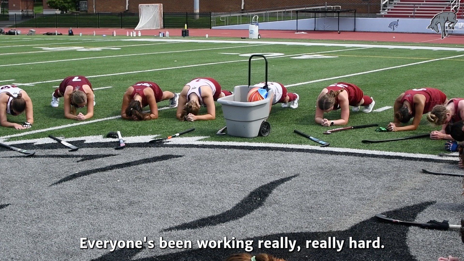 field hockey players in white and red jerseys stretching on a green turf field