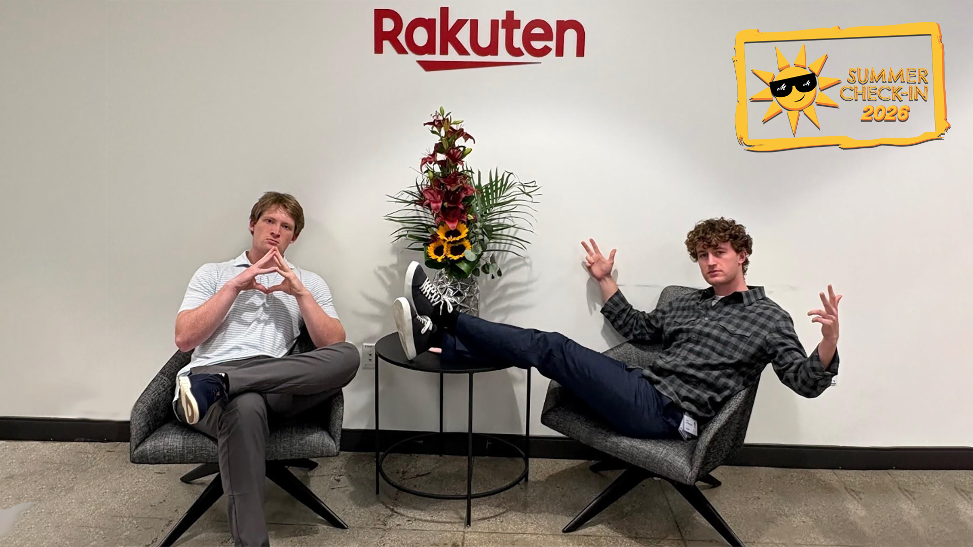 two young men sitting in office chairs with a plant in between them and the word Rakuten in red on the wall behind them 