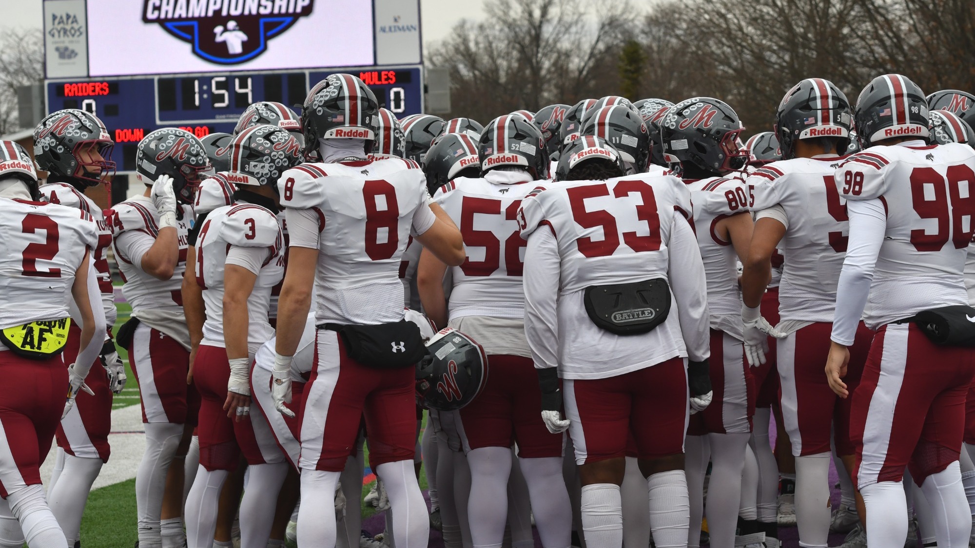 A group of football players clad in white uniforms huddles up