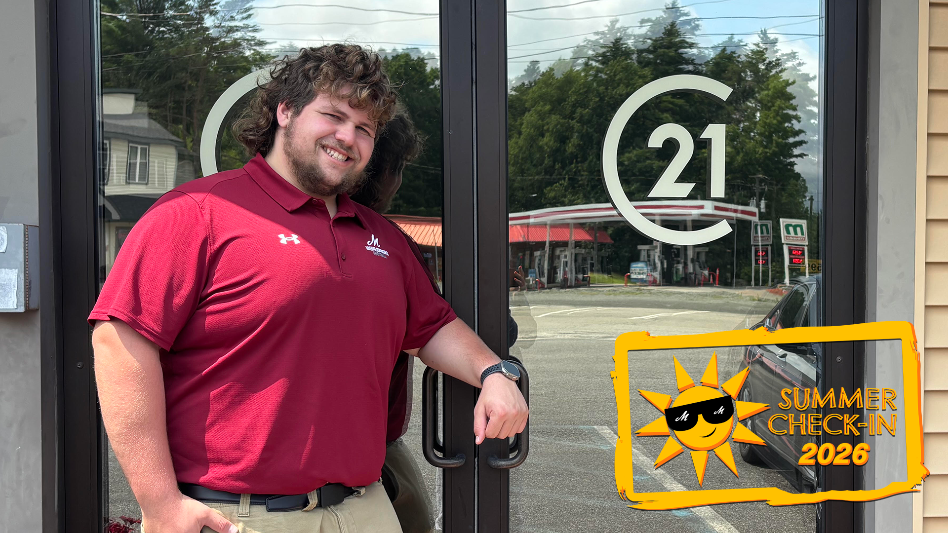 a young man in a maroon polo shirt posing outside in front of mirrored double doors with C21 on them