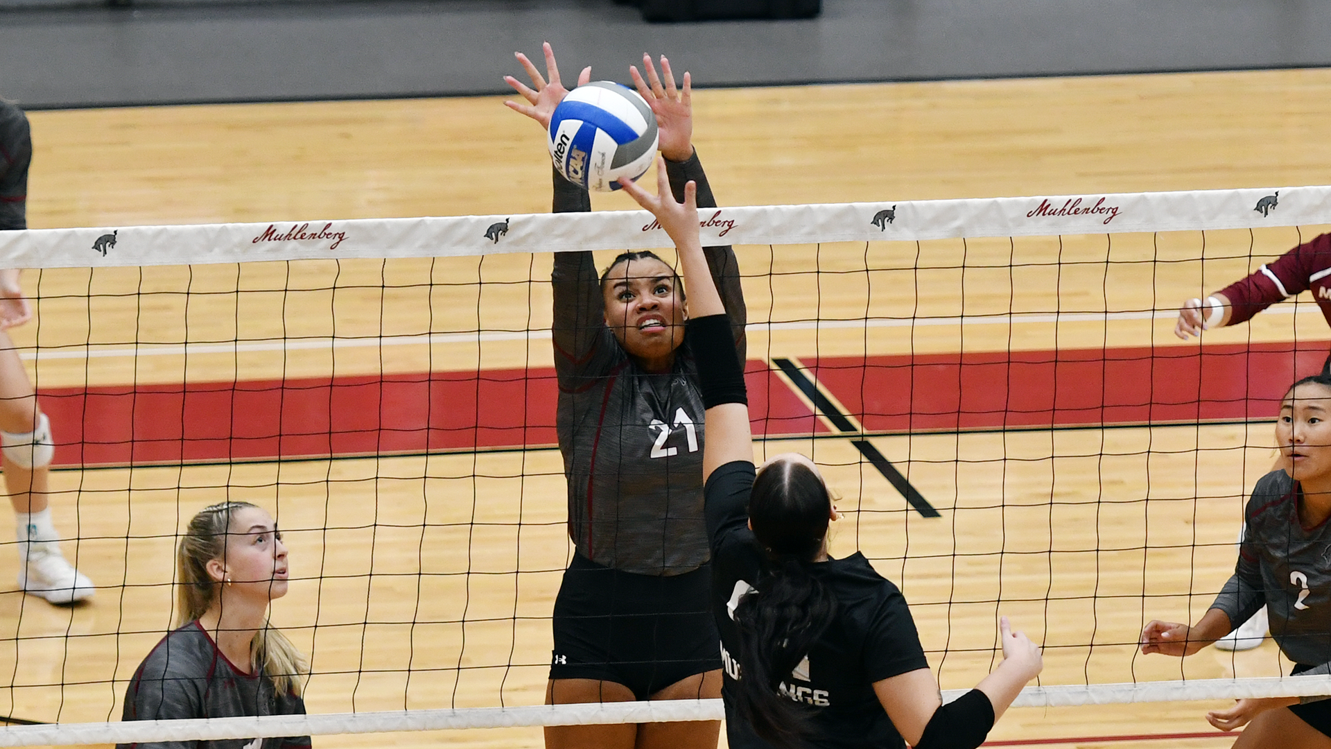 a volleyball player in a grey jersey leaping to block the ball over the net