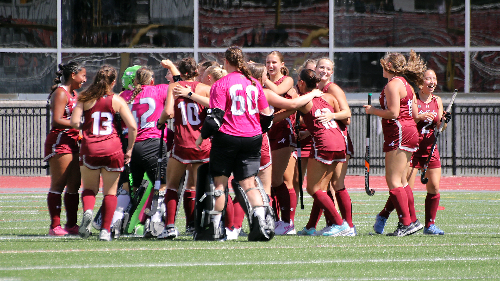field hockey players in red jersey celebrate on a turf field