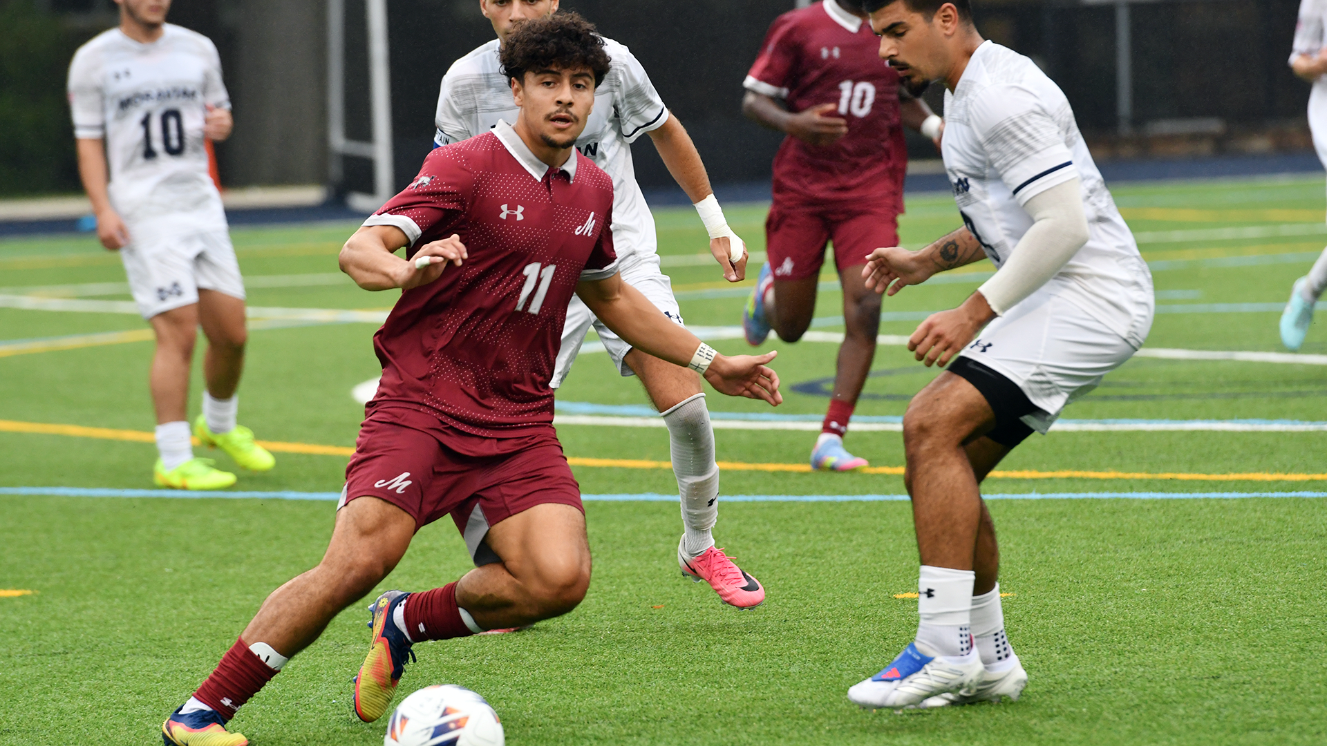 a men's soccer player in a red uniform dribbling between two players in white uniforms