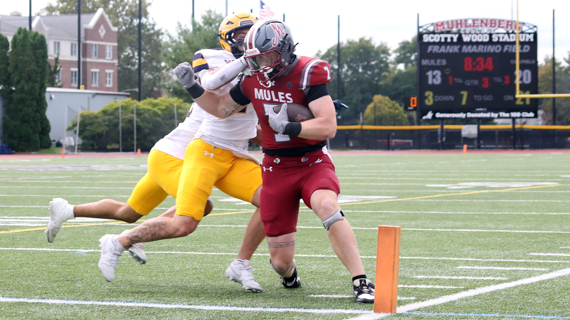 a football player in a red jersey and silver helmet carrying the ball into the end zone while a player in a white jersey and yellow helmet tries to tackle him