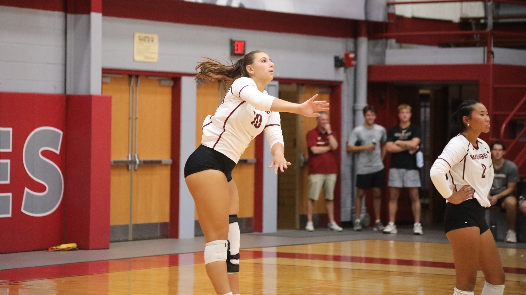 A volleyball player in a white uniform follows through after a serve on a volleyball court