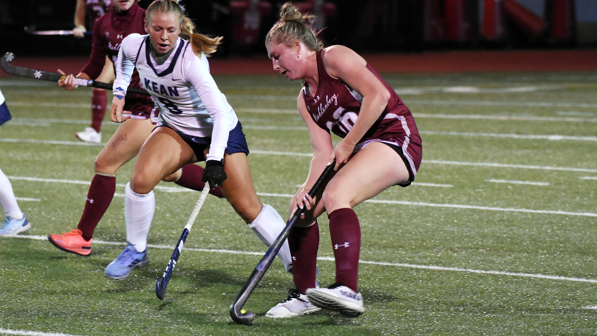 a field hockey player in a red uniform controlling the ball with her stick while being guarded by a player in a white uniform