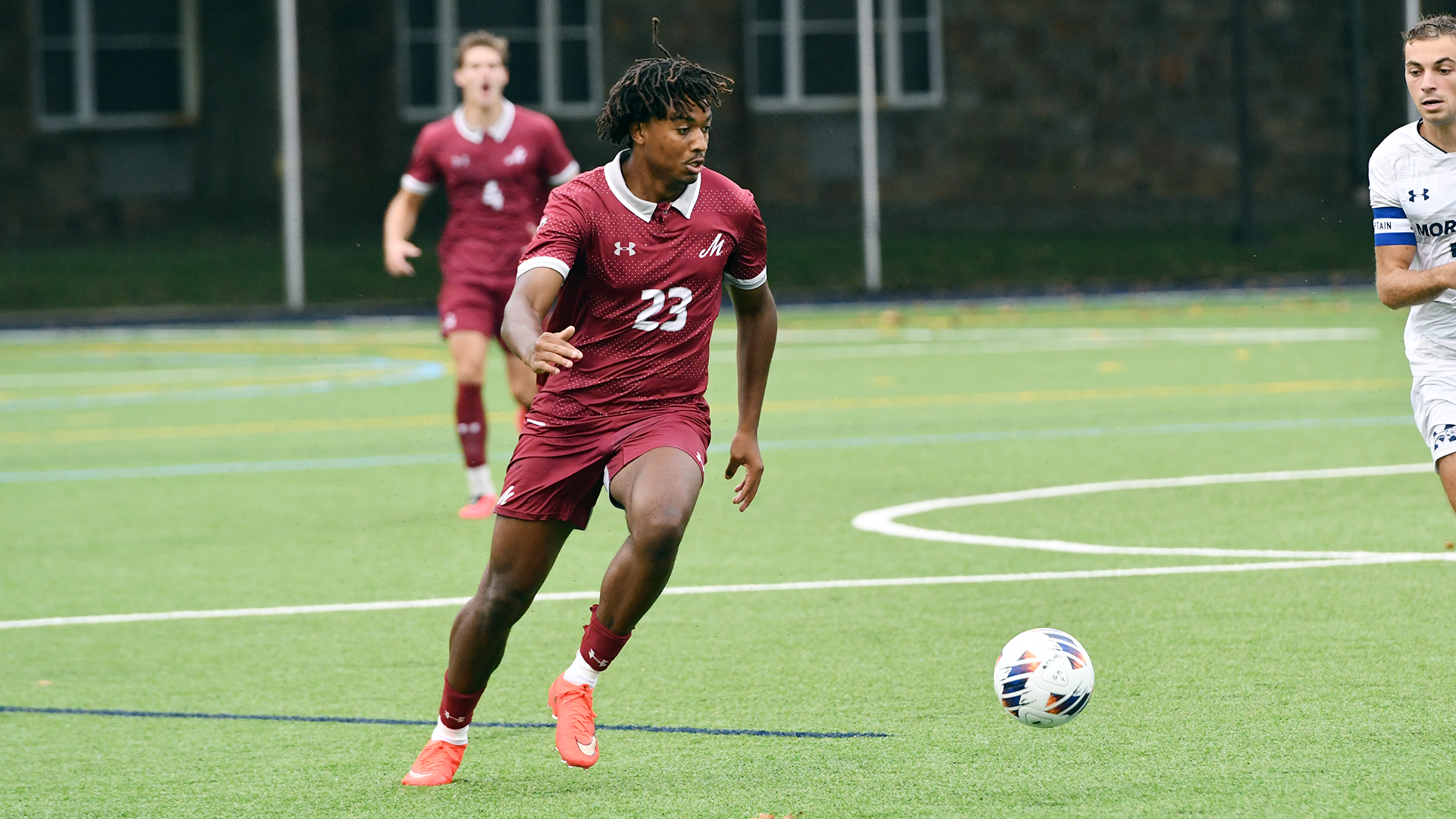 a soccer player in a red uniform dribbles on a green turf field