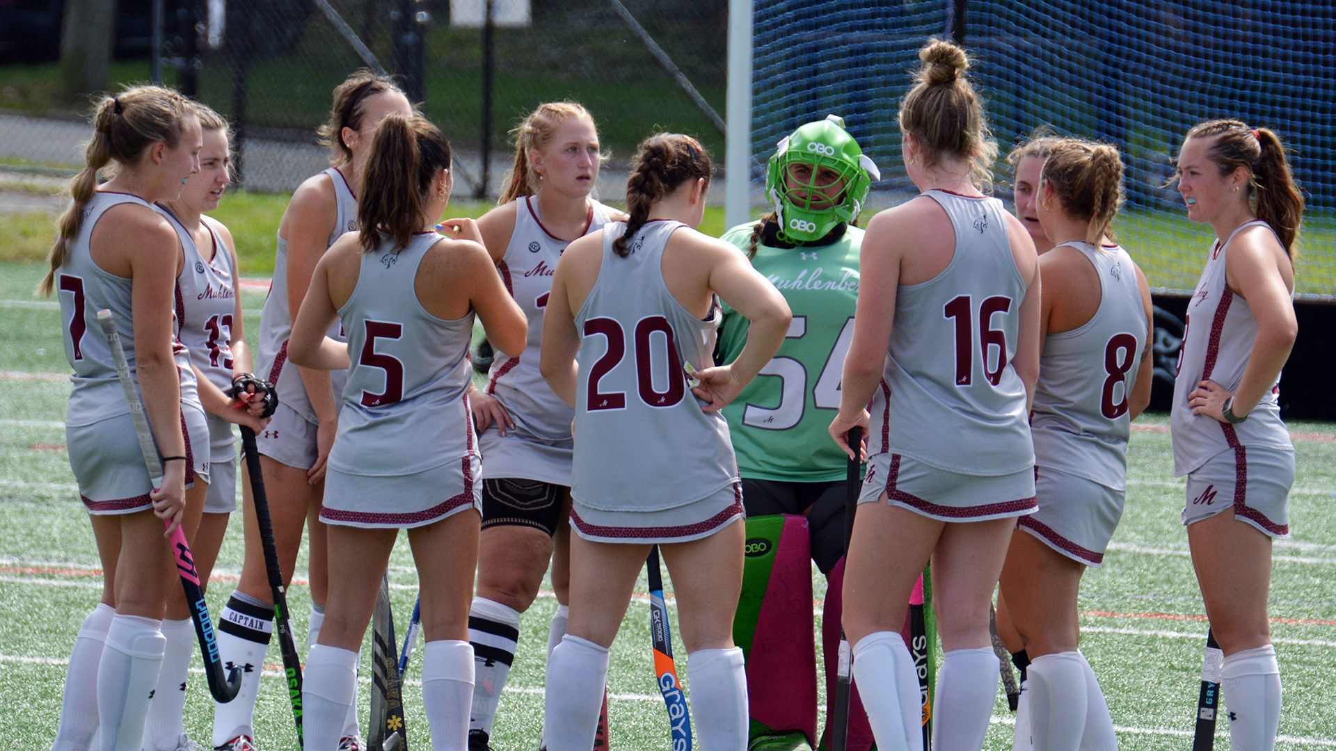 field hockey players in grey uniforms standing in a circle